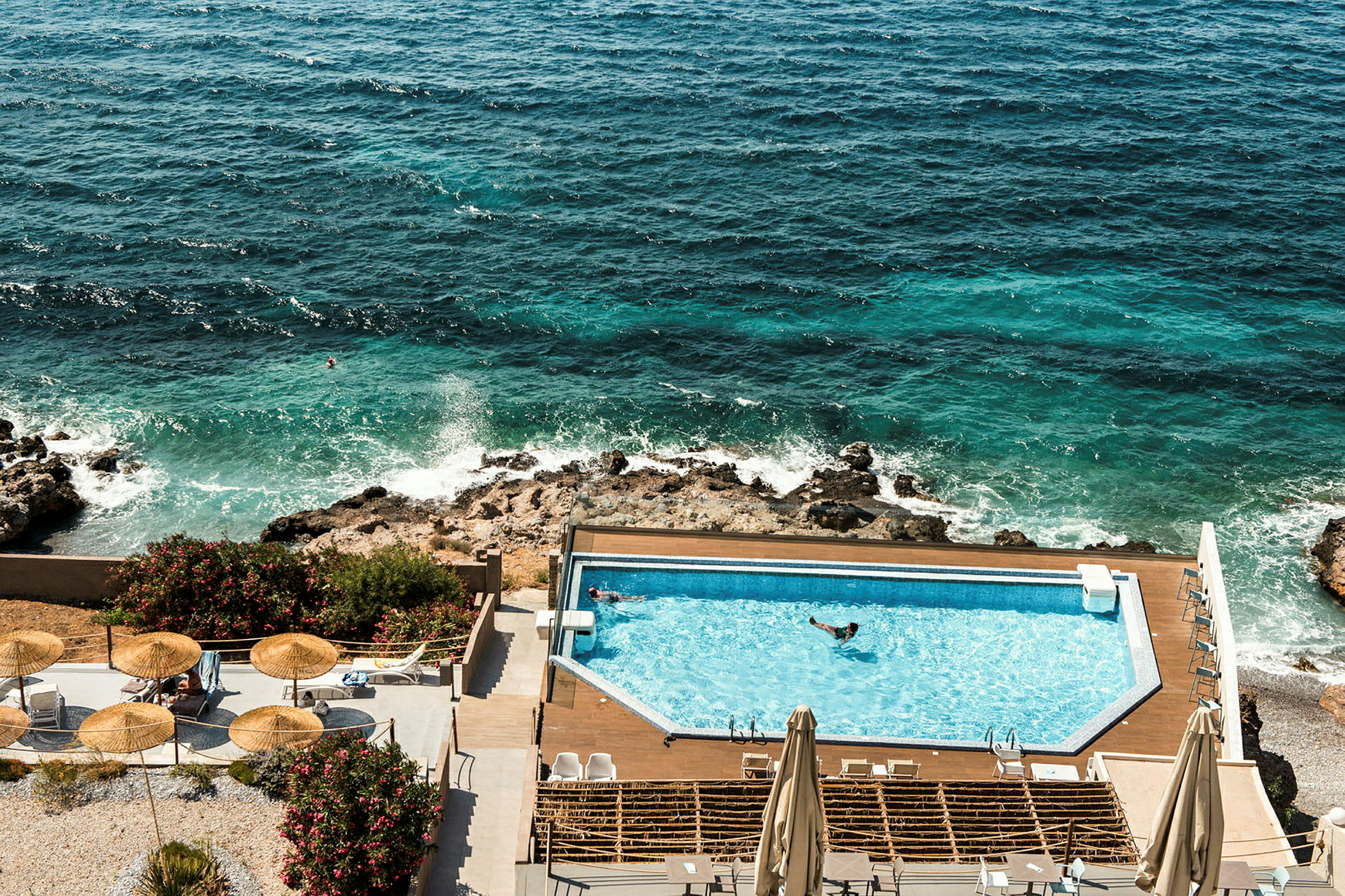 Vy över en hotellpool vid havet med solstolar och parasoller. (AI-genererad text)