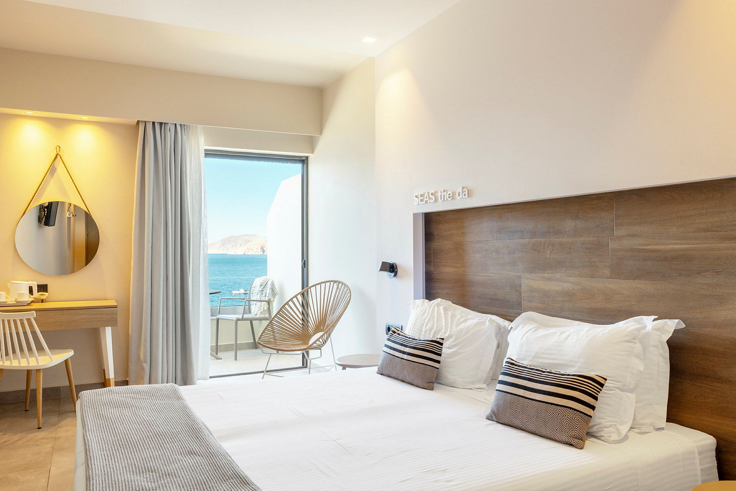 Ett hotellrum med en modern inredning, en dubbelsäng, ett skrivbord och en utsikt över havet från en balkong. (AI-genererad text)
