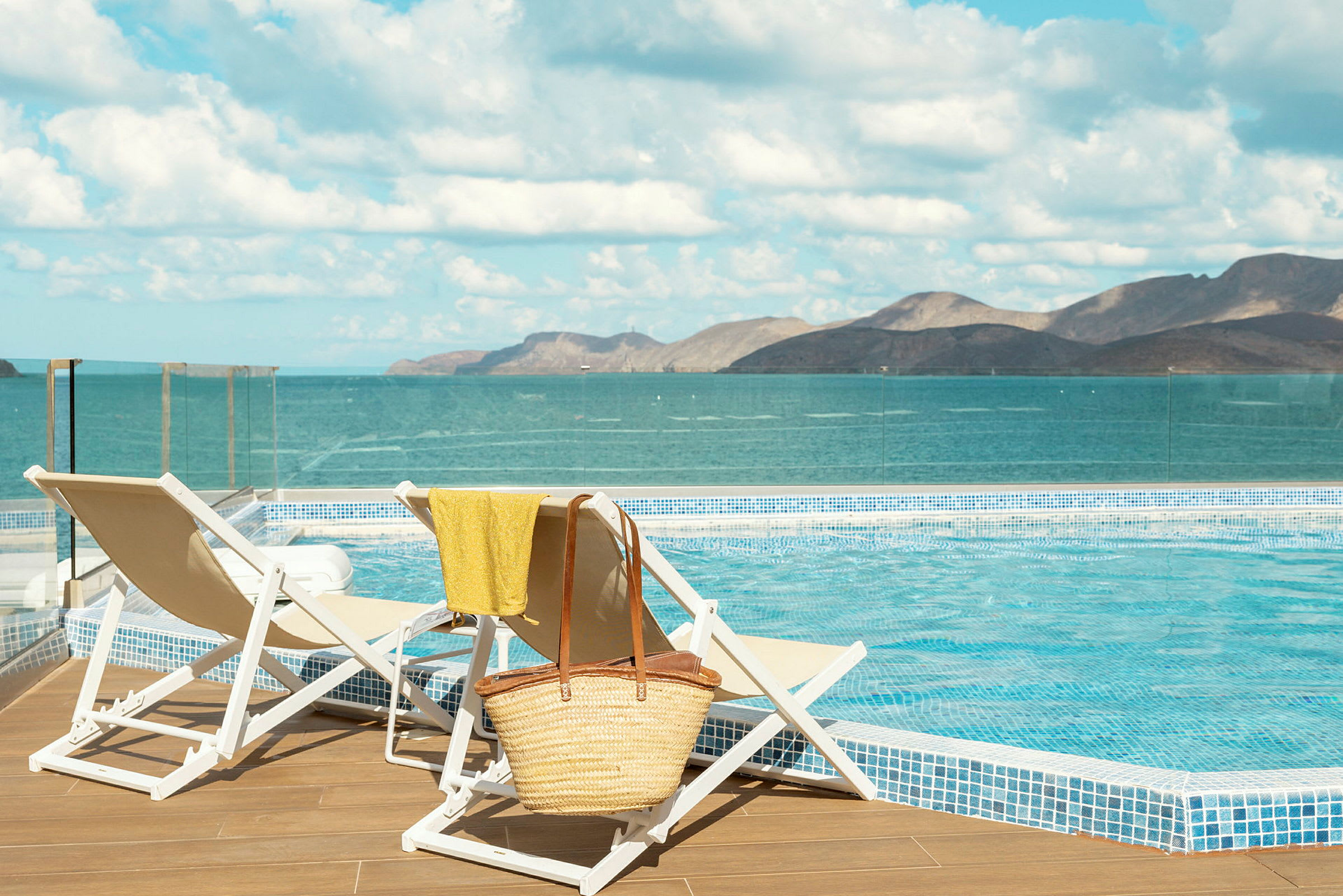 Två solstolar vid en pool med utsikt över havet och berg i bakgrunden. (AI-genererad text)