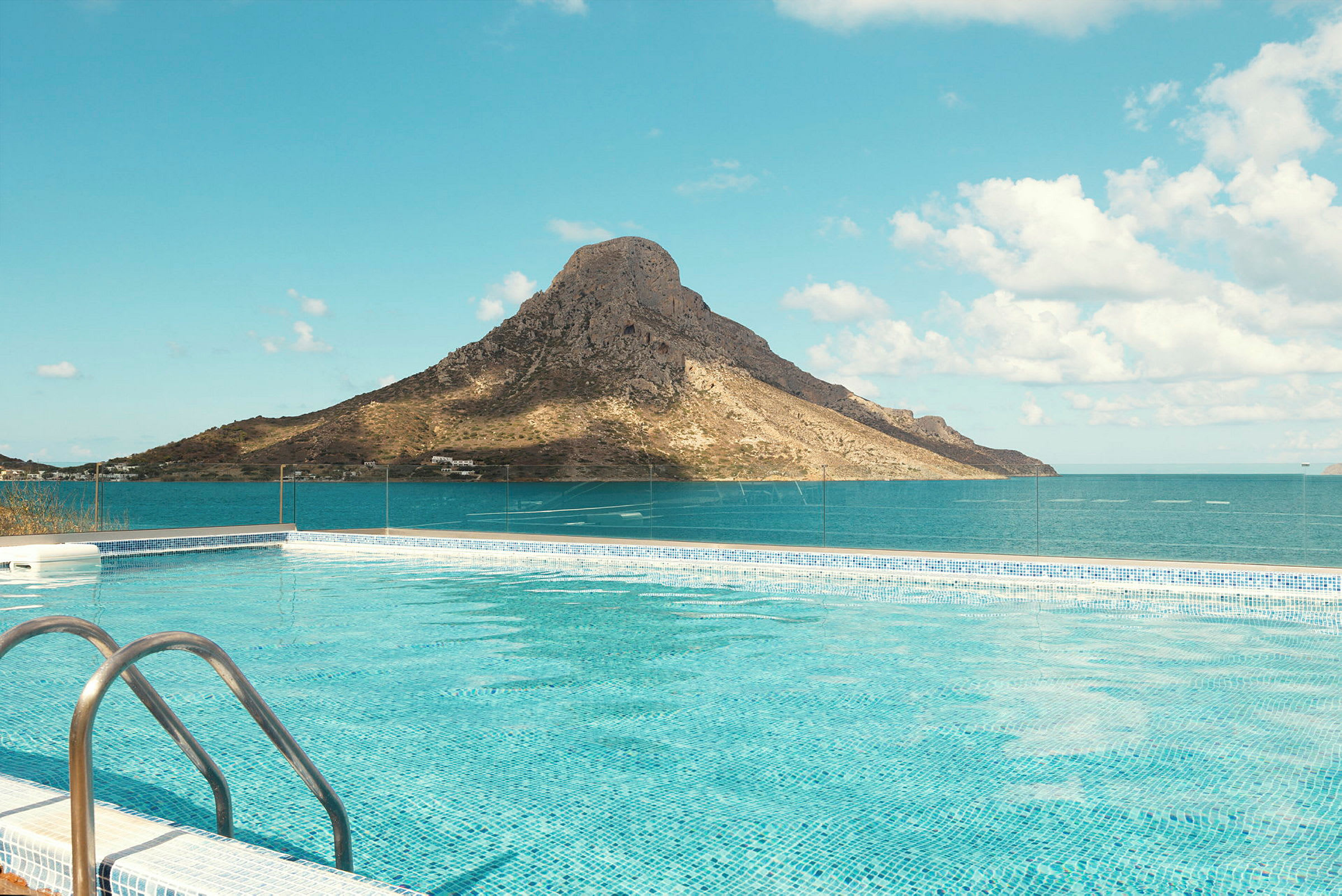 En pool med klart blått vatten framför ett berg vid havet under en klar himmel. (AI-genererad text)