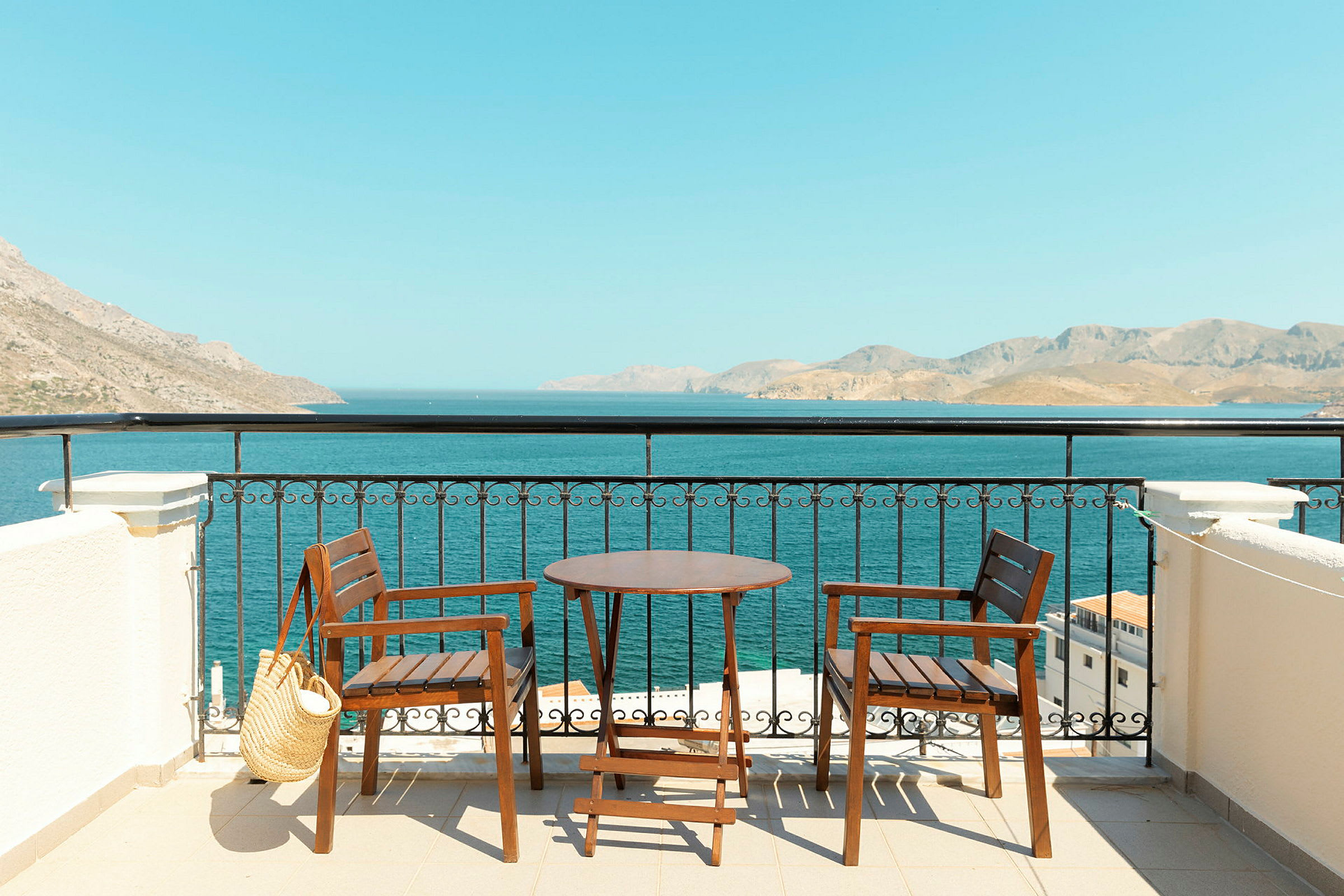 Två trästolar och ett bord på en terrass med utsikt över havet och berg i fjärran. (AI-genererad text)