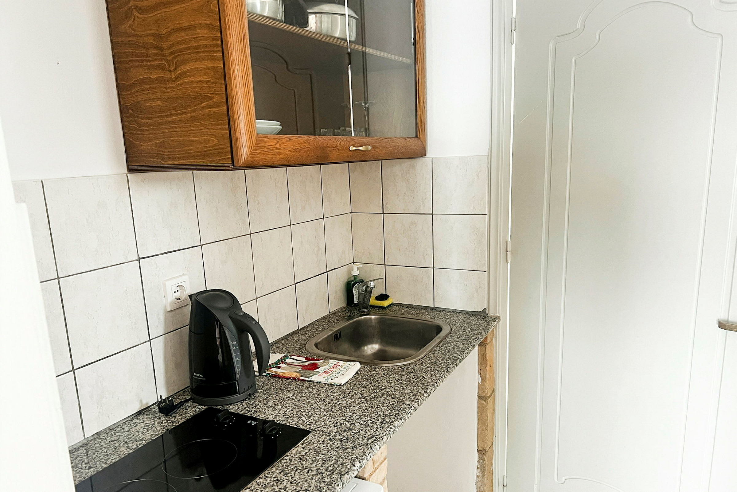Ett litet kök med en diskbänk, en induktionshäll, en vattenkokare och ett väggskåp. (AI-genererad text)