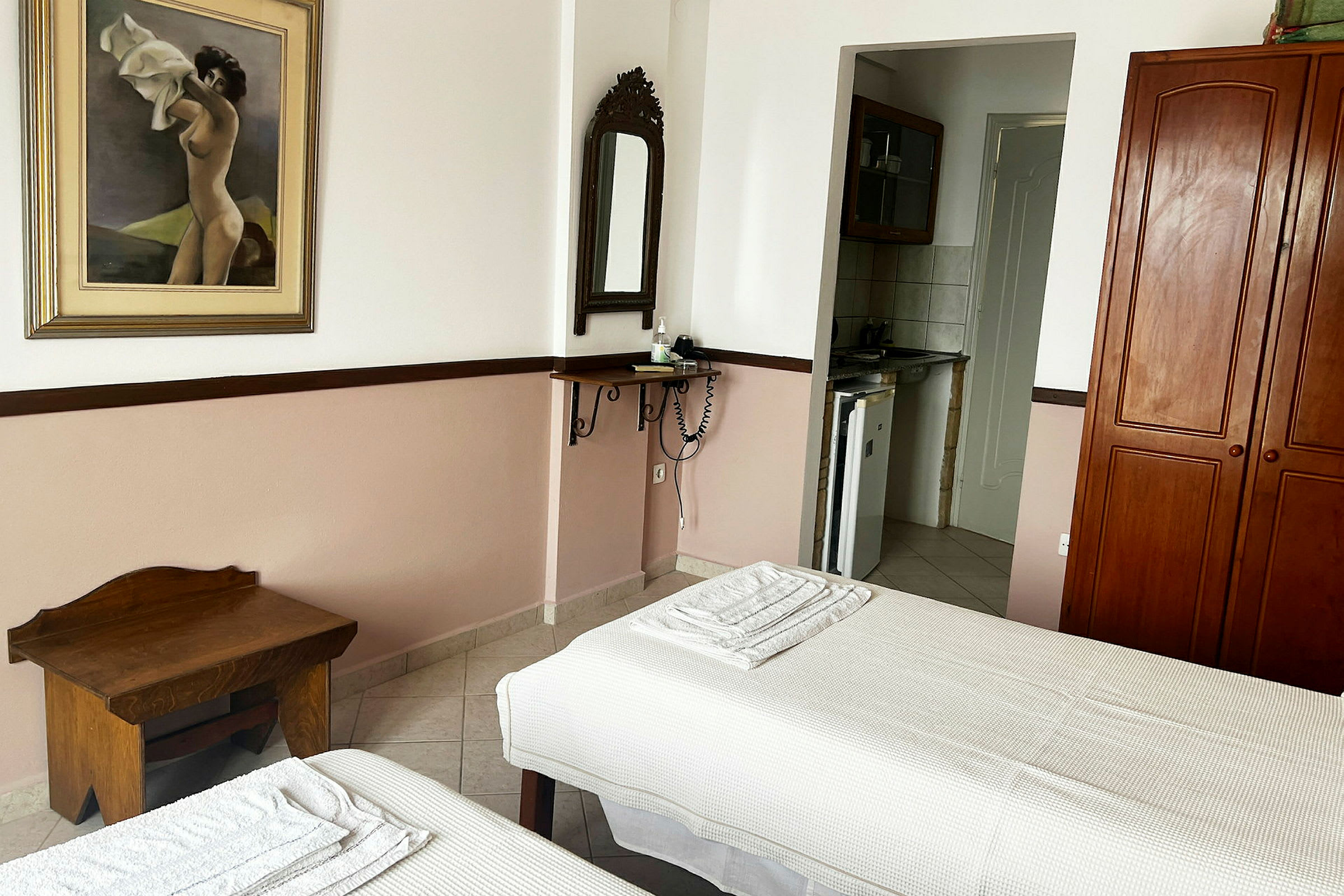 Ett hotellrum med två enkelsängar, en målning på väggen och en liten köksdel. (AI-genererad text)