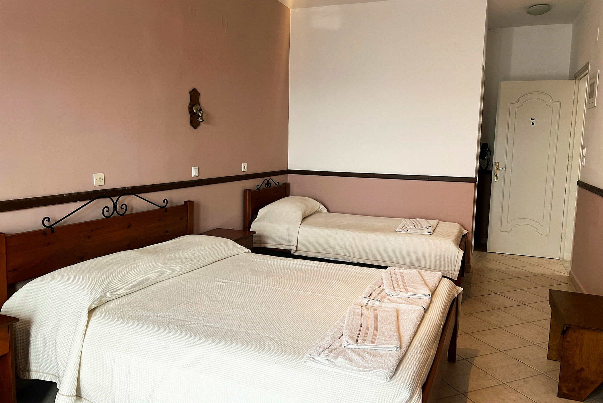 Ett hotellrum med två bäddar, enkel inredning med ljusa väggar och golv. (AI-genererad text)
