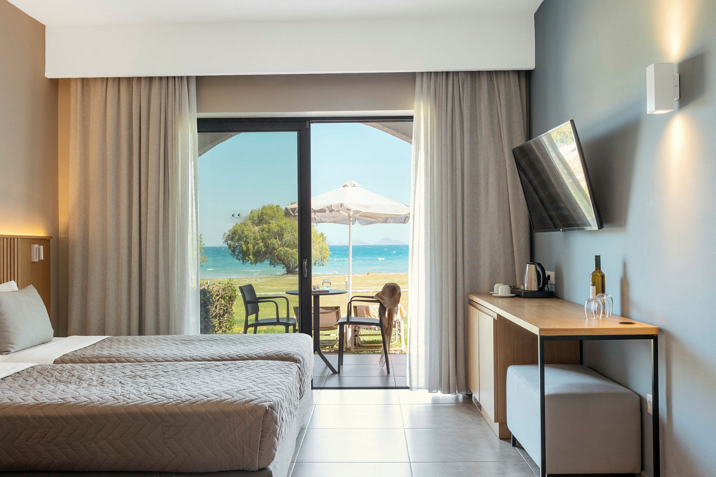 Hotellrum med två enkelsängar, en öppning mot en möblerad terrass och havsutsikt. (AI-genererad text)