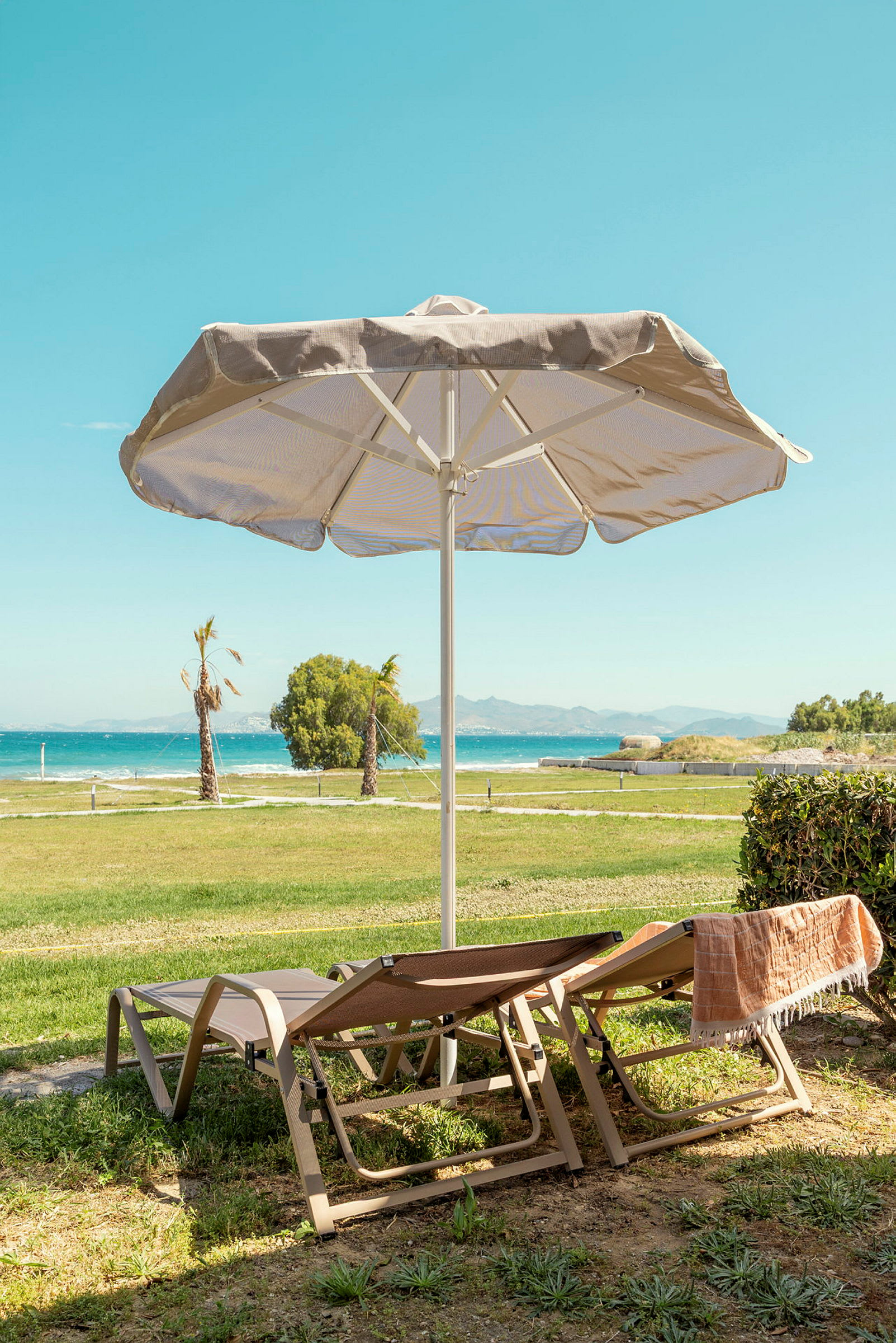 Två solstolar står under ett parasoll med utsikt mot havet och grönska. (AI-genererad text)