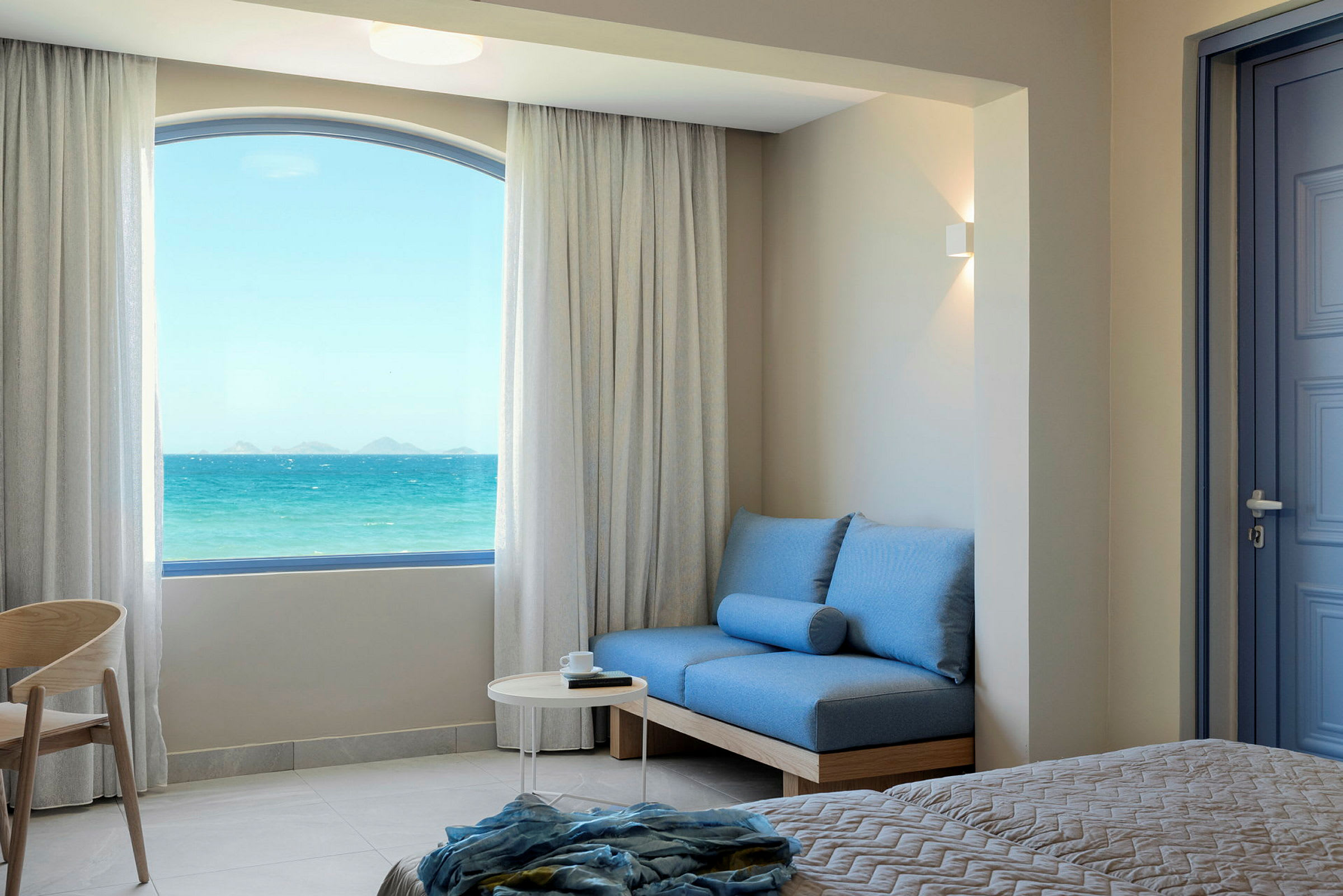 Hotellrum med havsutsikt genom ett stort fönster. (AI-genererad text)