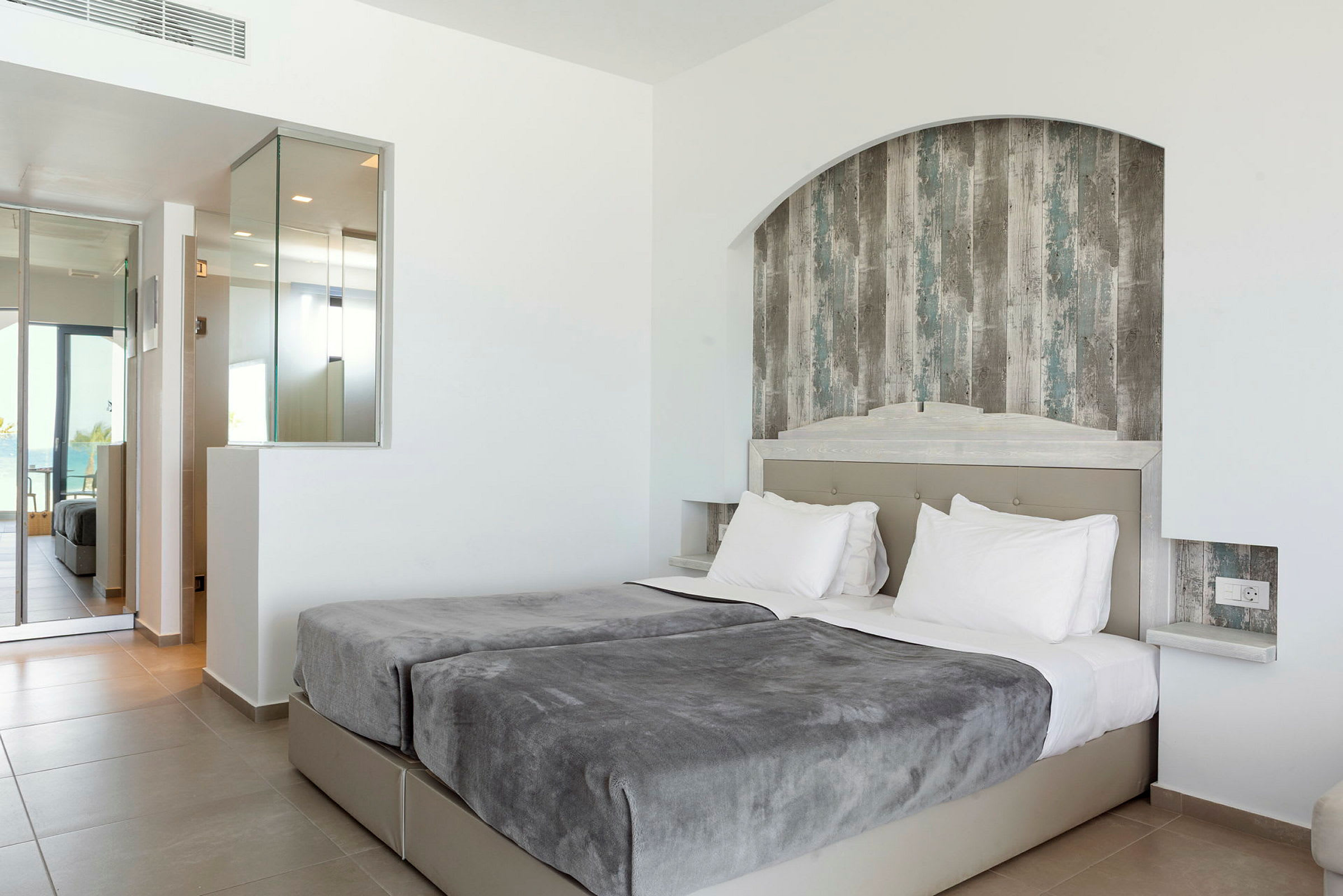 Ett hotellrum med två sängar, gråa överkast och vitkalkade väggar. (AI-genererad text)