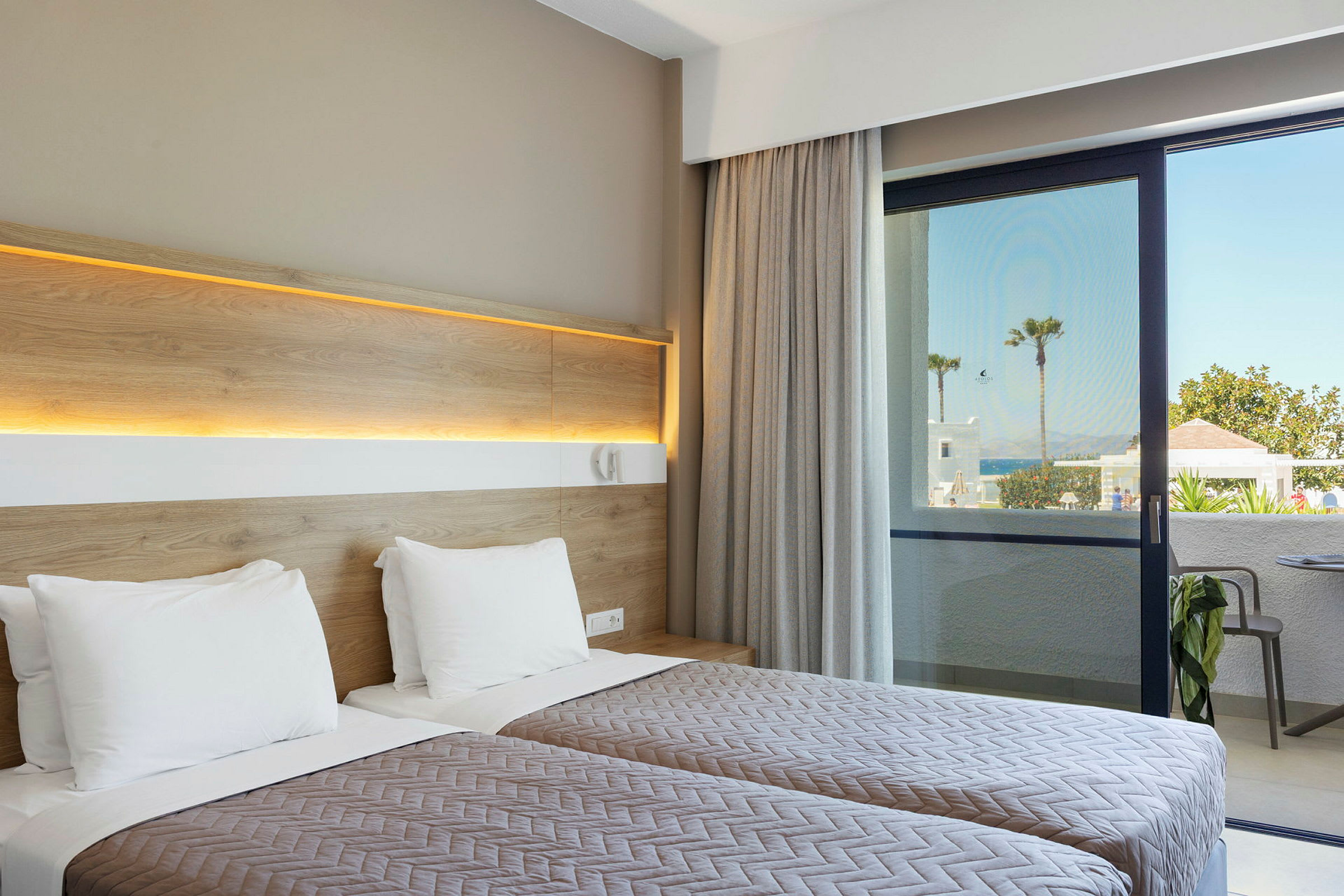 Hotellrum med två enkelsängar och utsikt mot en uteplats och hav i bakgrunden. (AI-genererad text)