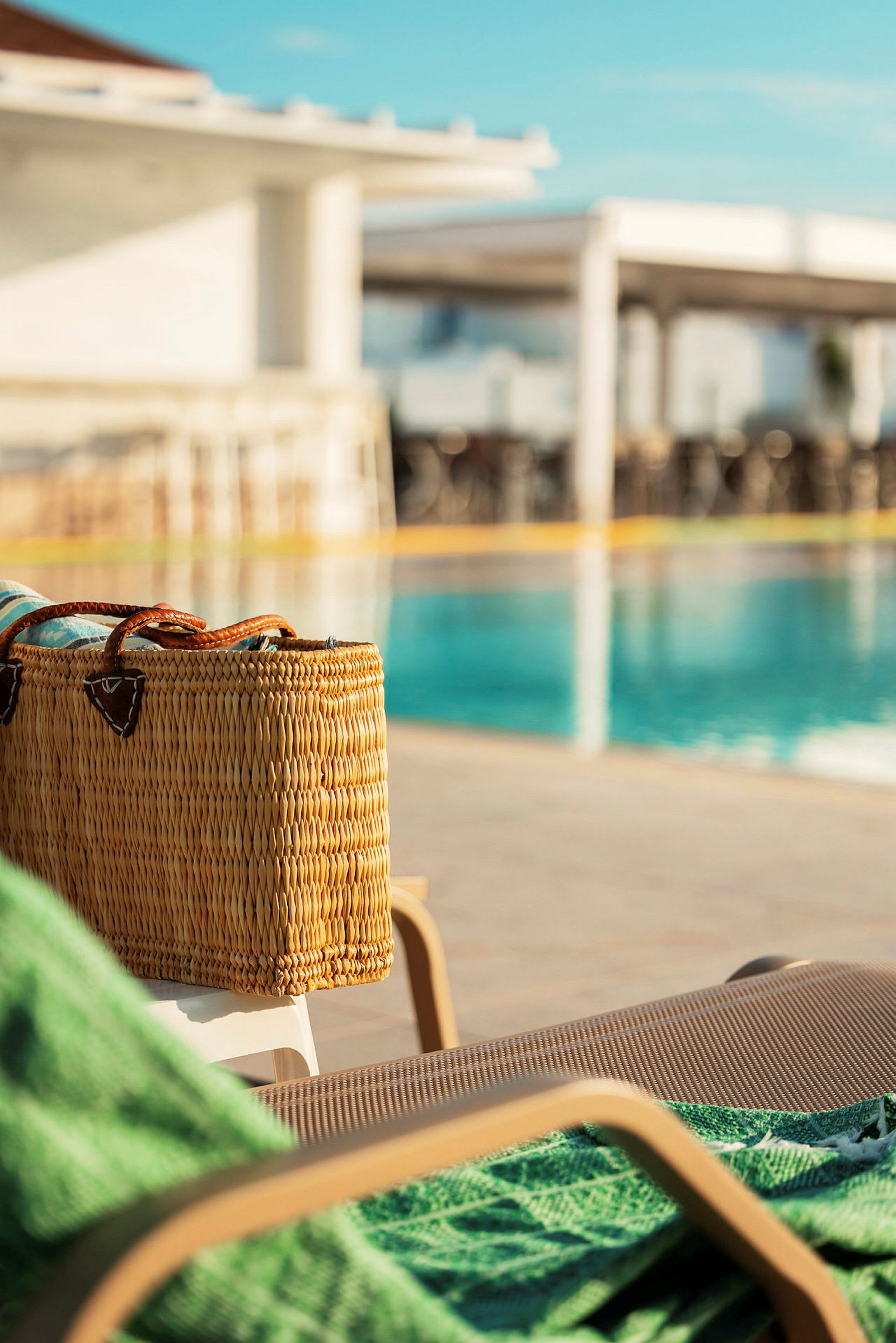En närbild av en solstol med en korgväska och grön handduk vid en pool. (AI-genererad text)
