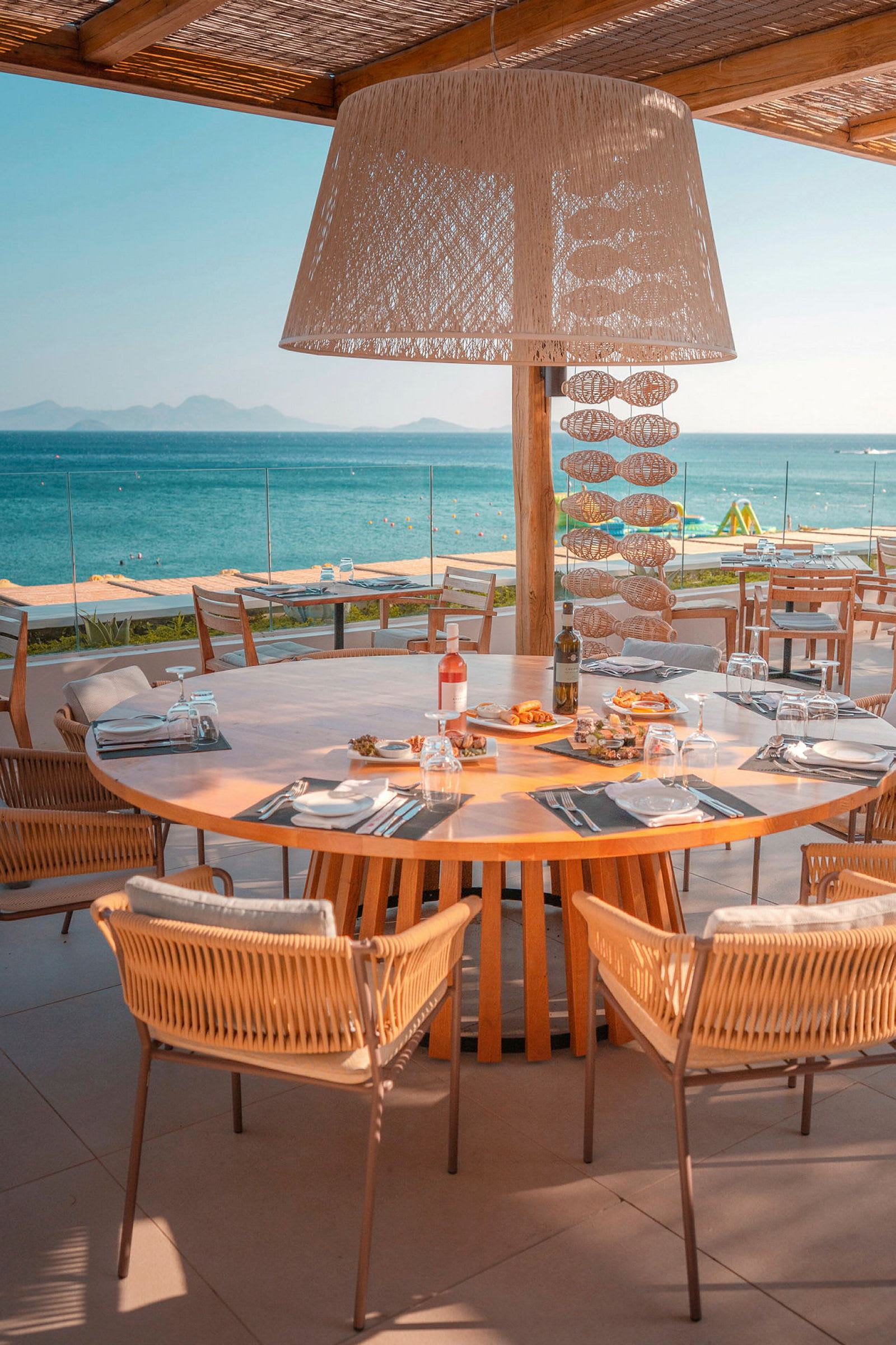 En dukad träbord med stolar vid en restaurangterrass som vetter mot havet. (AI-genererad text)