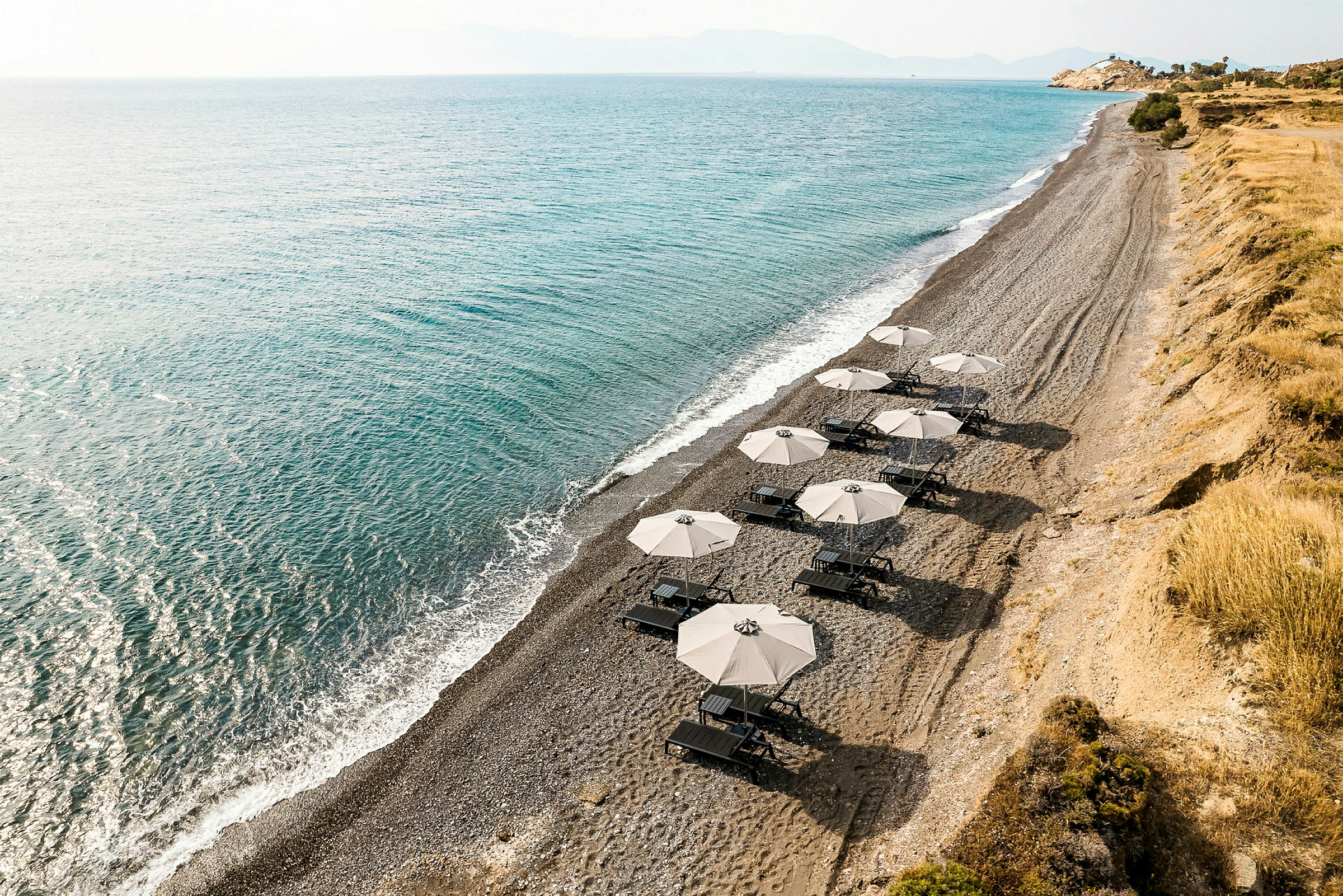 En stenstrand med parasoller och solstolar vid havet. (AI-genererad text)