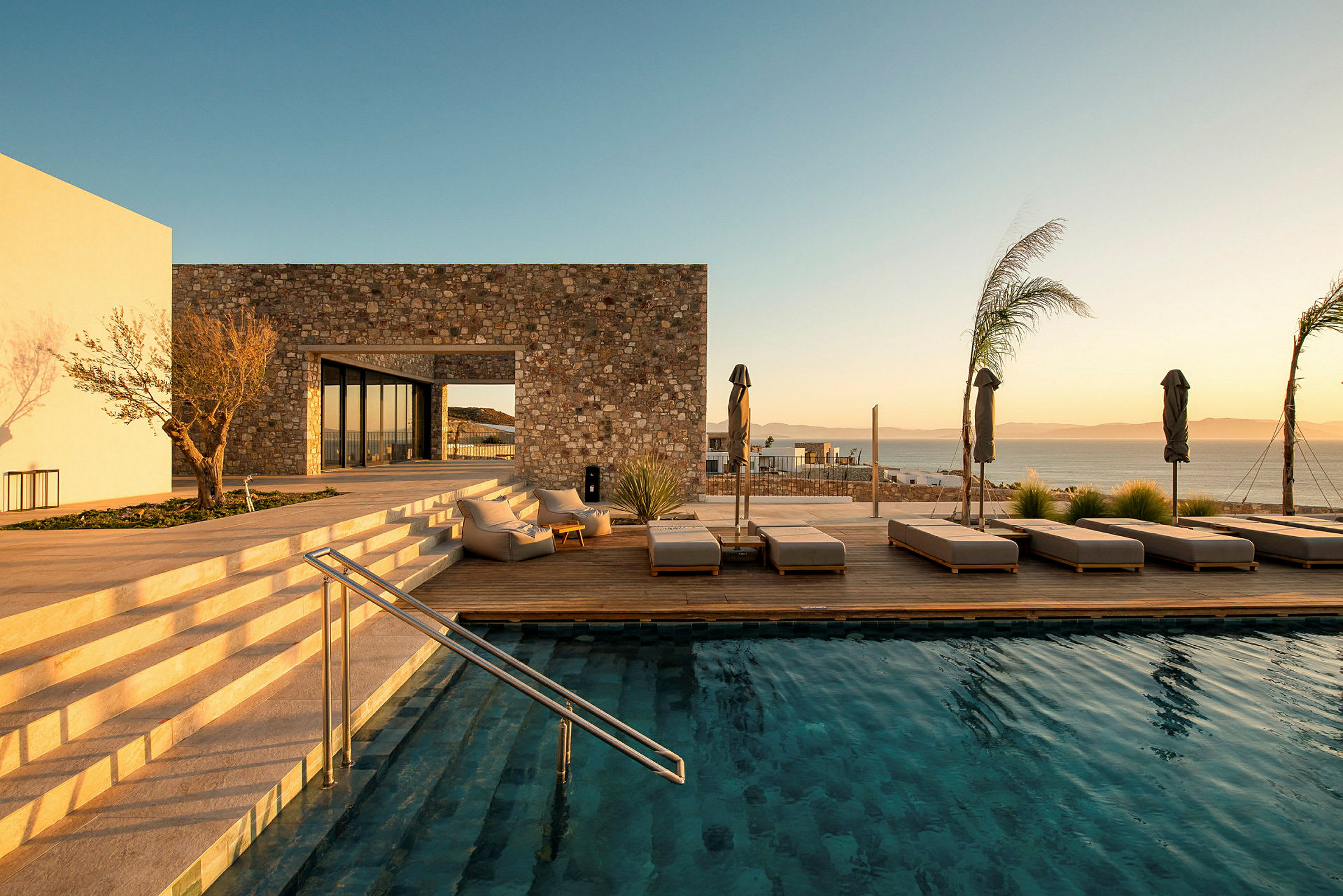 En stenbyggnad med modern pool och solstolar vid havet. (AI-genererad text)