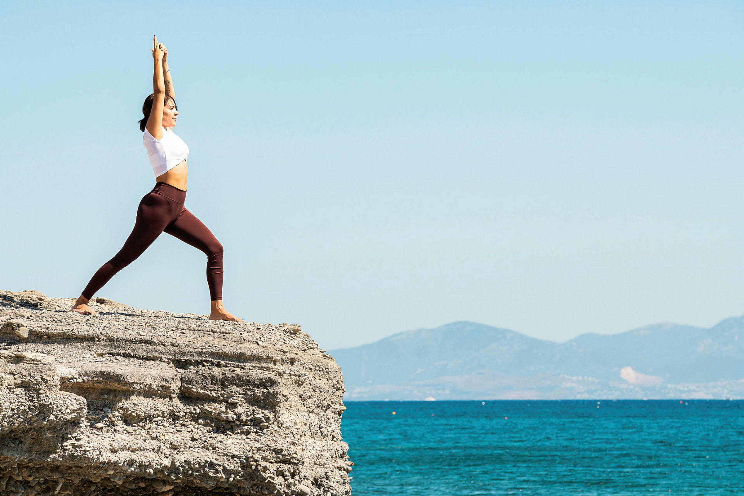 En person gör yoga på en klippa vid havet med berg i bakgrunden. (AI-genererad text)
