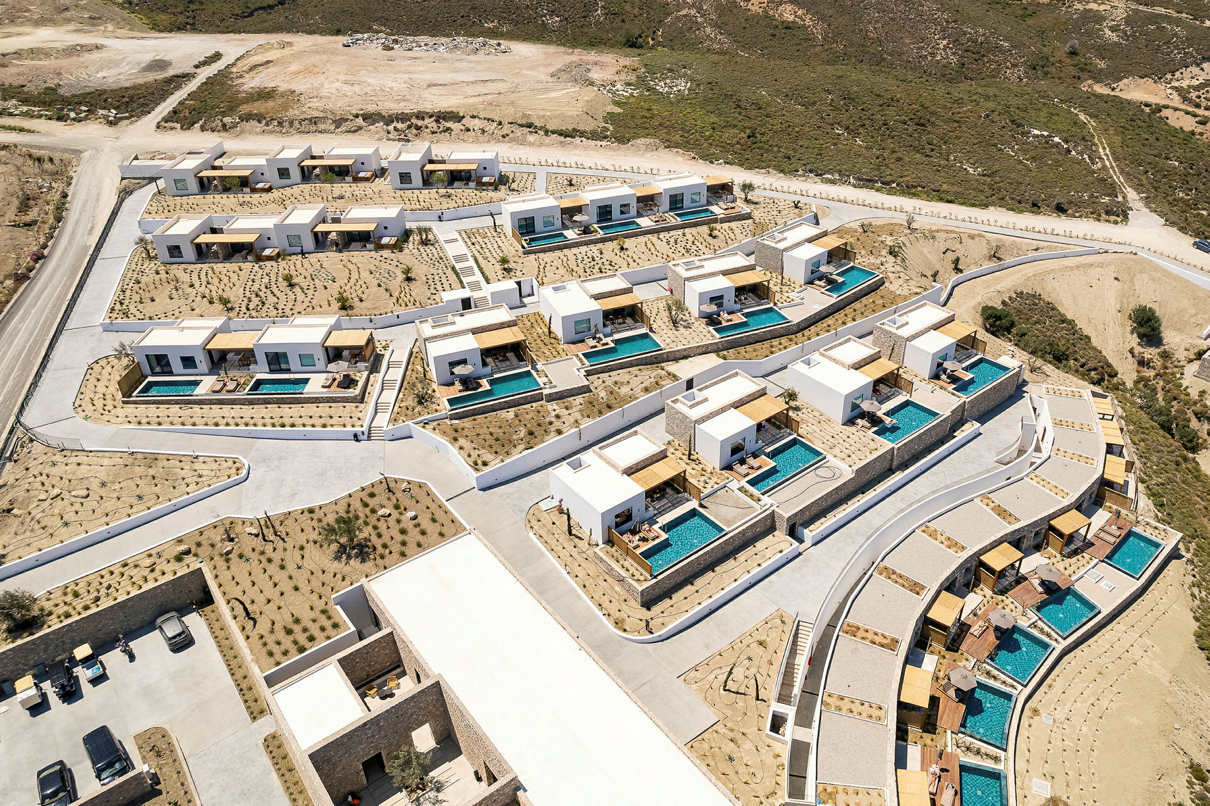 Flygfoto av en resort med moderna hus och privata pooler omgivna av karga landskap. (AI-genererad text)