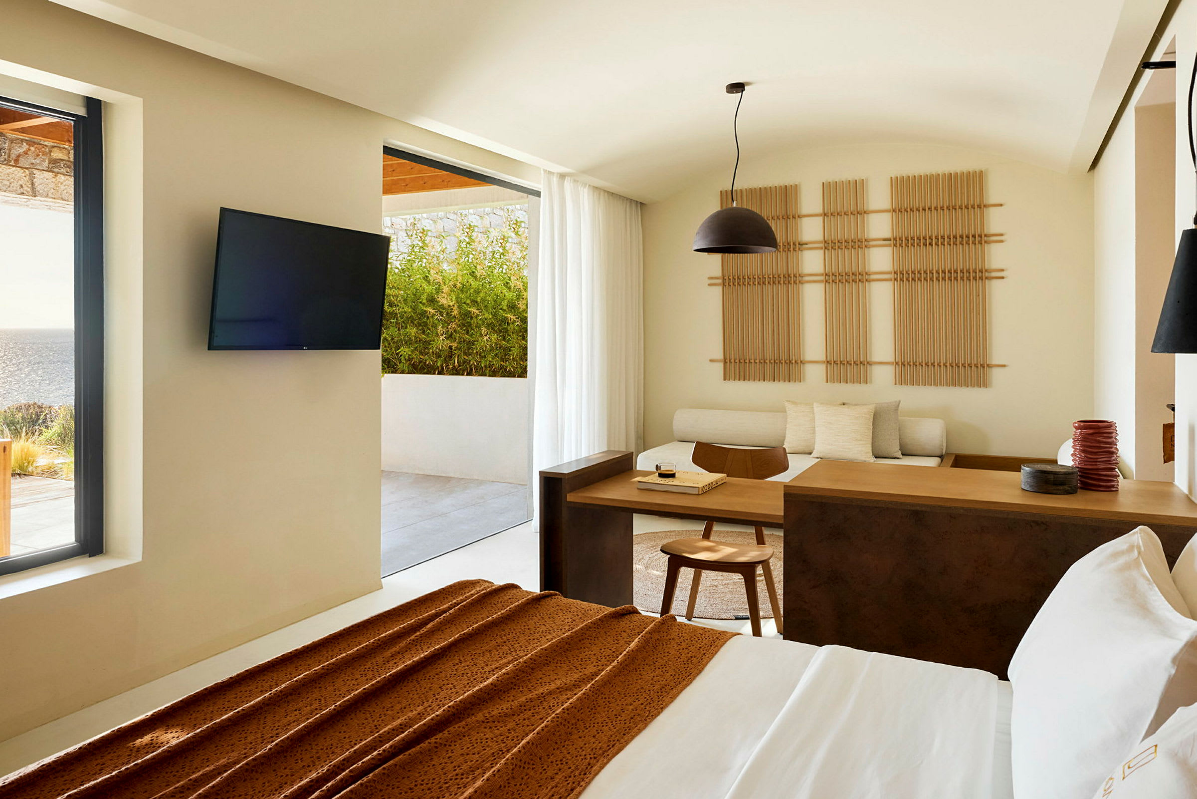Ett modernt hotellrum med utsikt mot en terrass och havet, inrett med minimalistiska möbler och ljusa färger. (AI-genererad text)