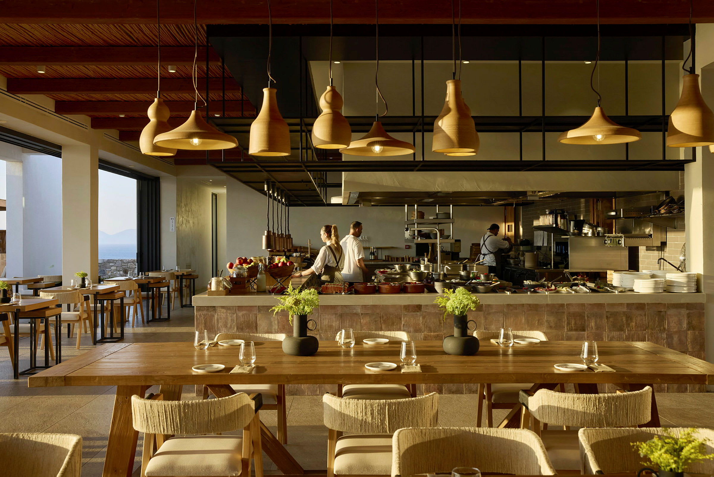 En modern restaurangmiljö med eleganta trä och ljusdesignsdetaljer, där kockar arbetar bakom en serveringsdisk. (AI-genererad text)