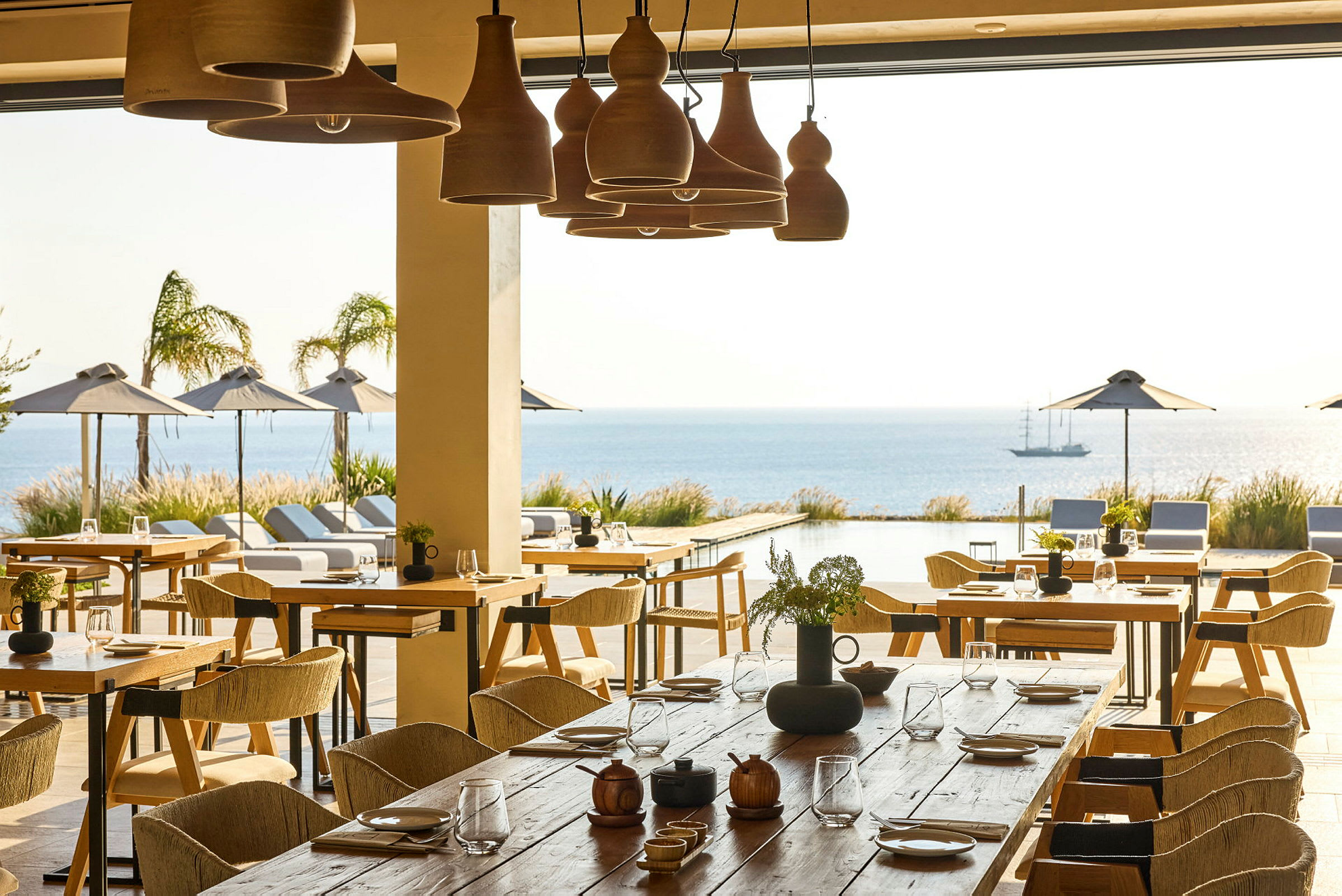 En restaurang med bord och stolar, med utsikt över en utomhuspool, havet och hängparasoller. (AI-genererad text)