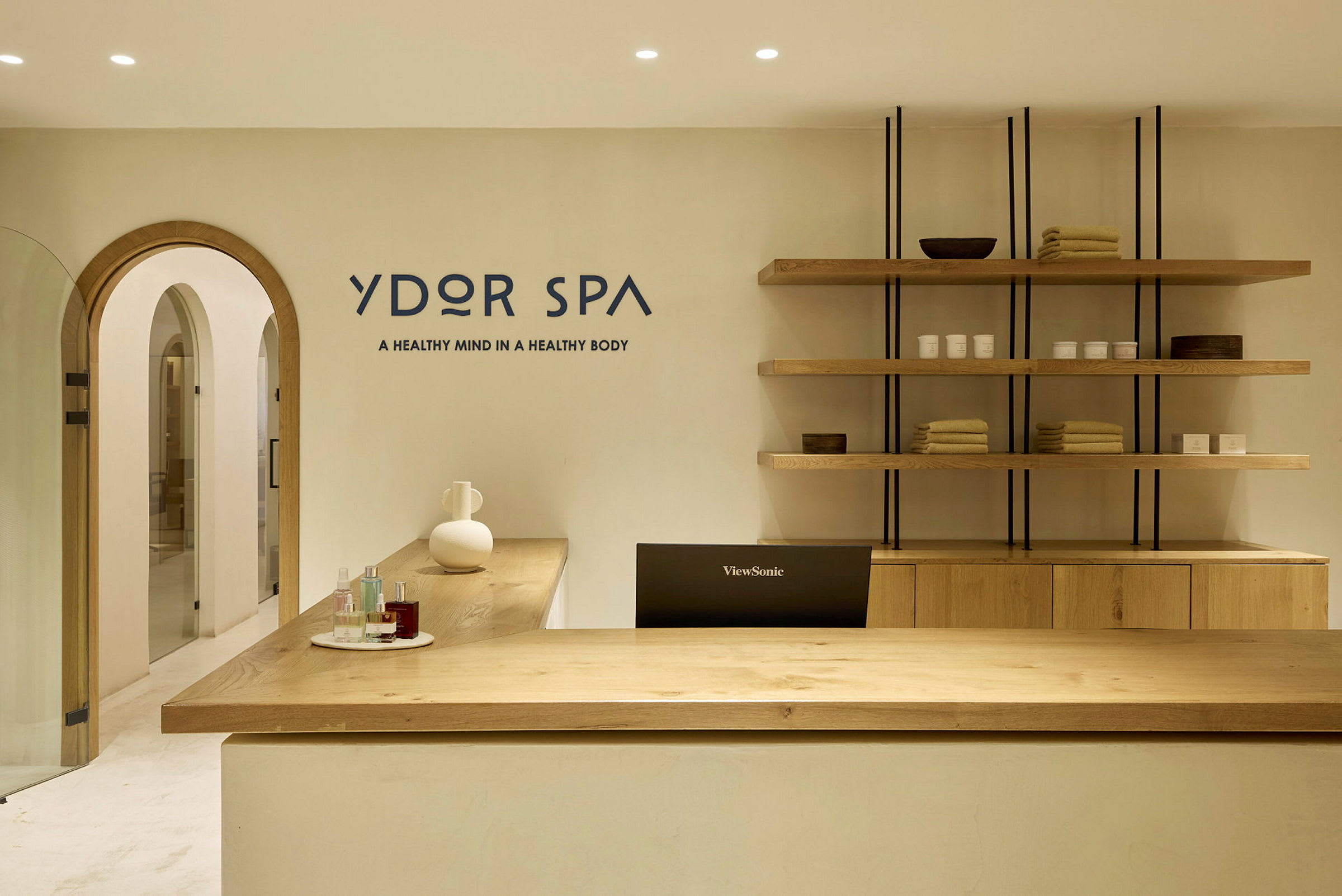 En receptionsdisk i ett spa med produkter och handdukar på hyllor bakom. (AI-genererad text)