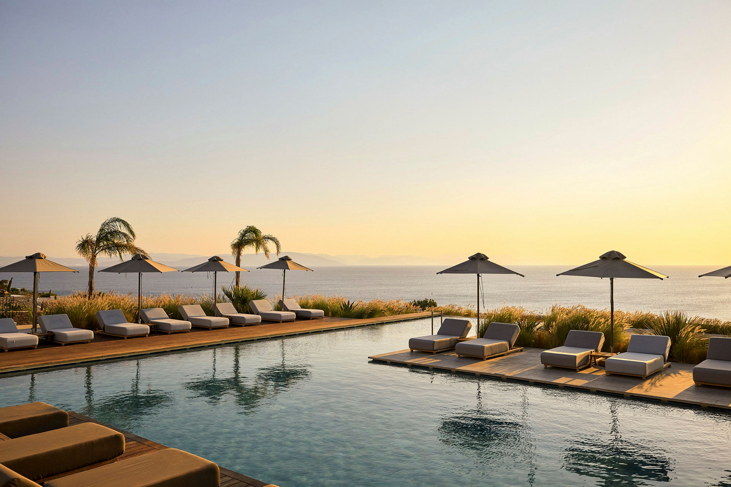 En infinitypool omgiven av solstolar och parasoller vid solnedgången, med en vy över havet. (AI-genererad text)