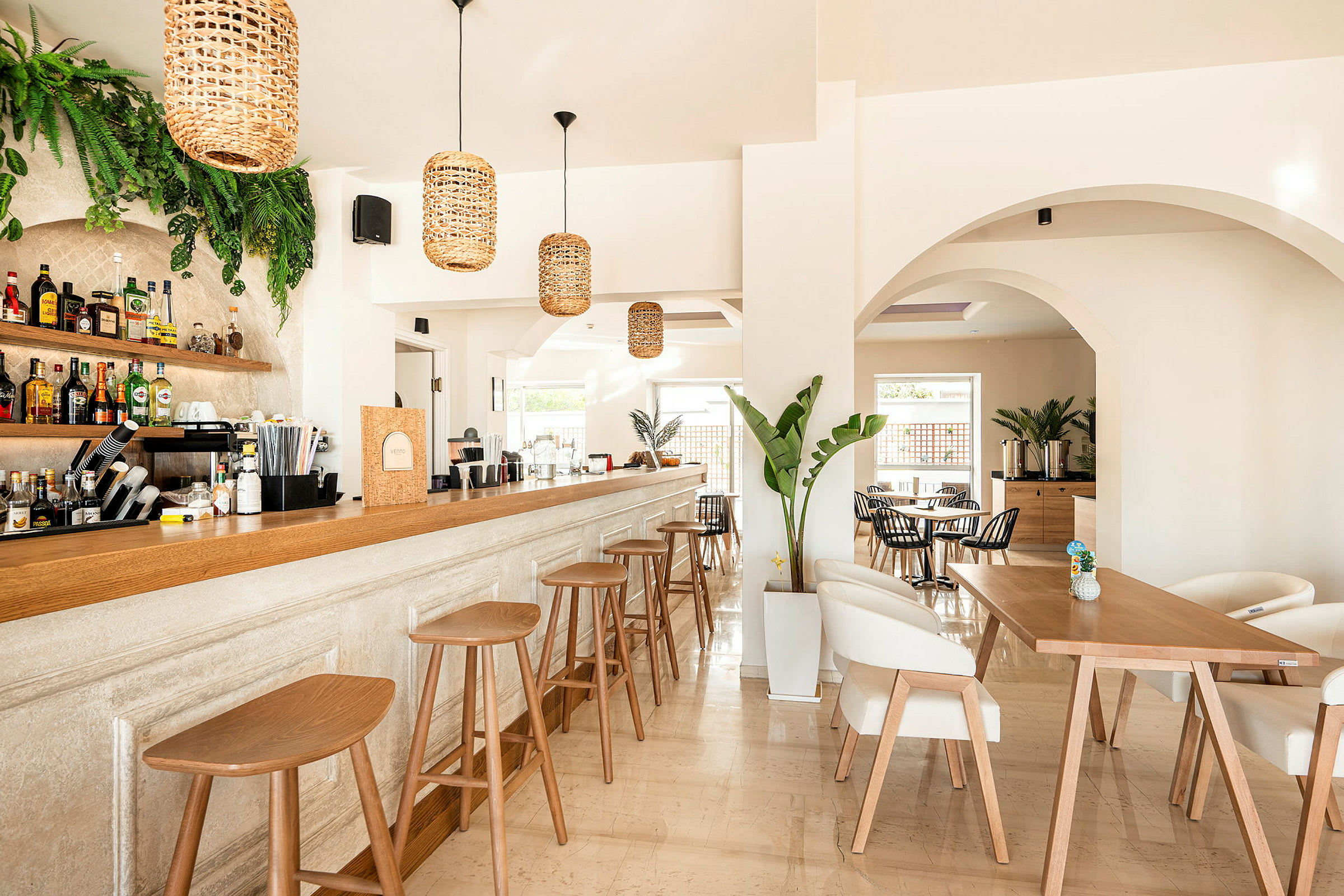En elegant inredd bar med moderna trästolar och ett långt räcke, omgiven av ljusa väggar och växtdekorationer. (AI-genererad text)