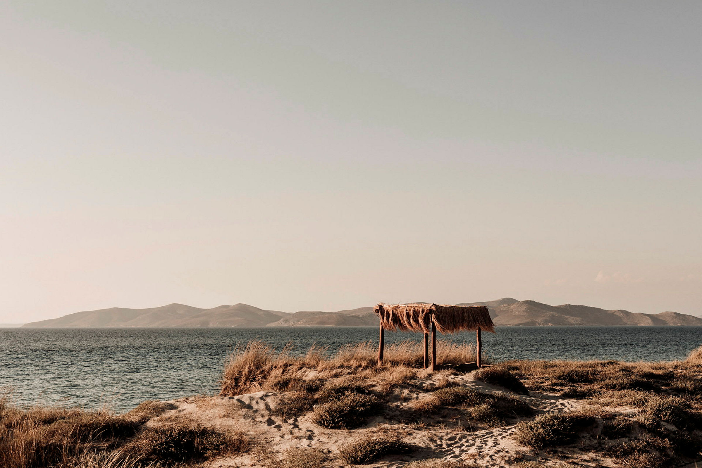 Ett strandlandskap med ett enkelt skydd av trä och halm vid havet. (AI-genererad text)