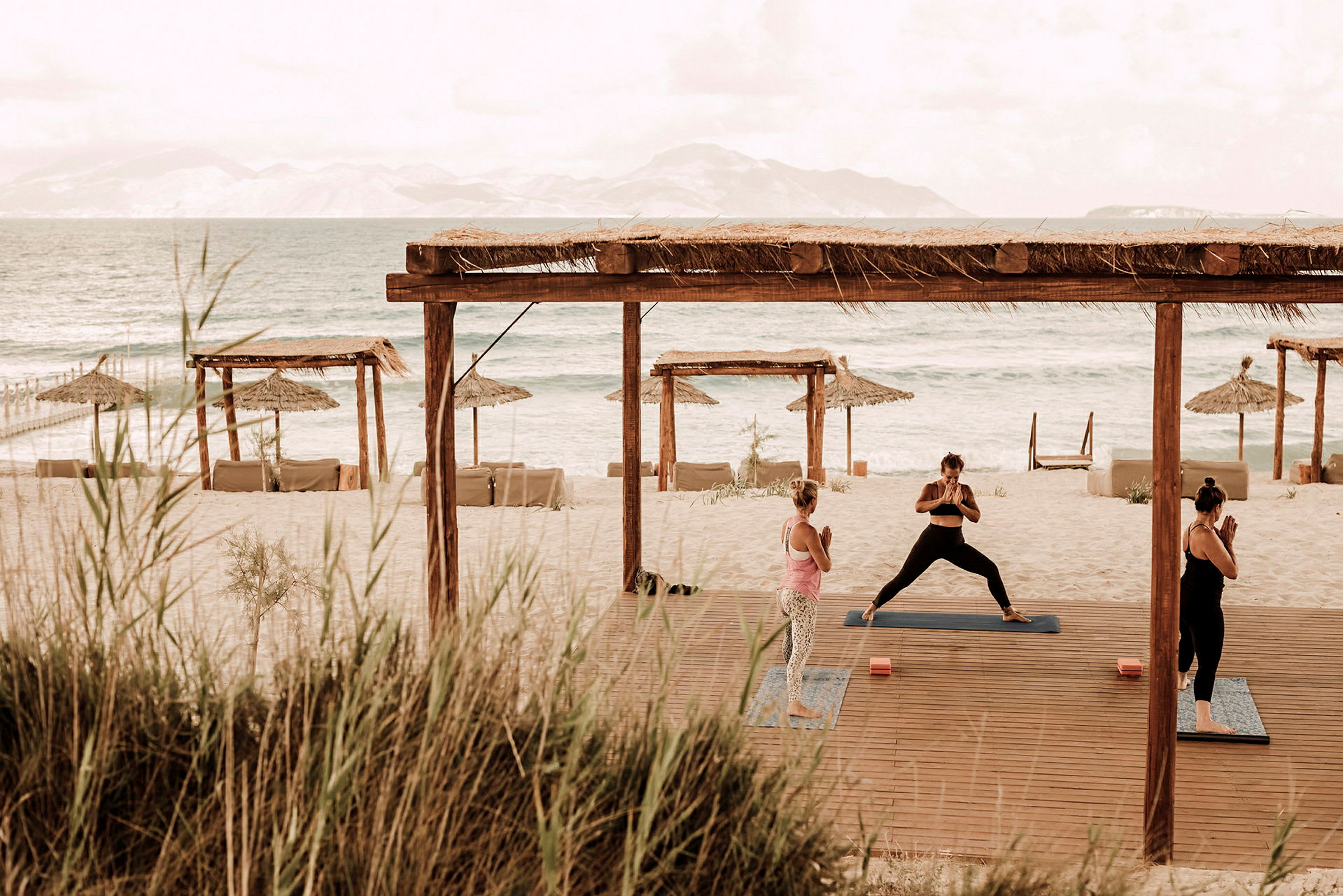Personer utför yoga på en strand med utsikt över havet och parasoller. (AI-genererad text)