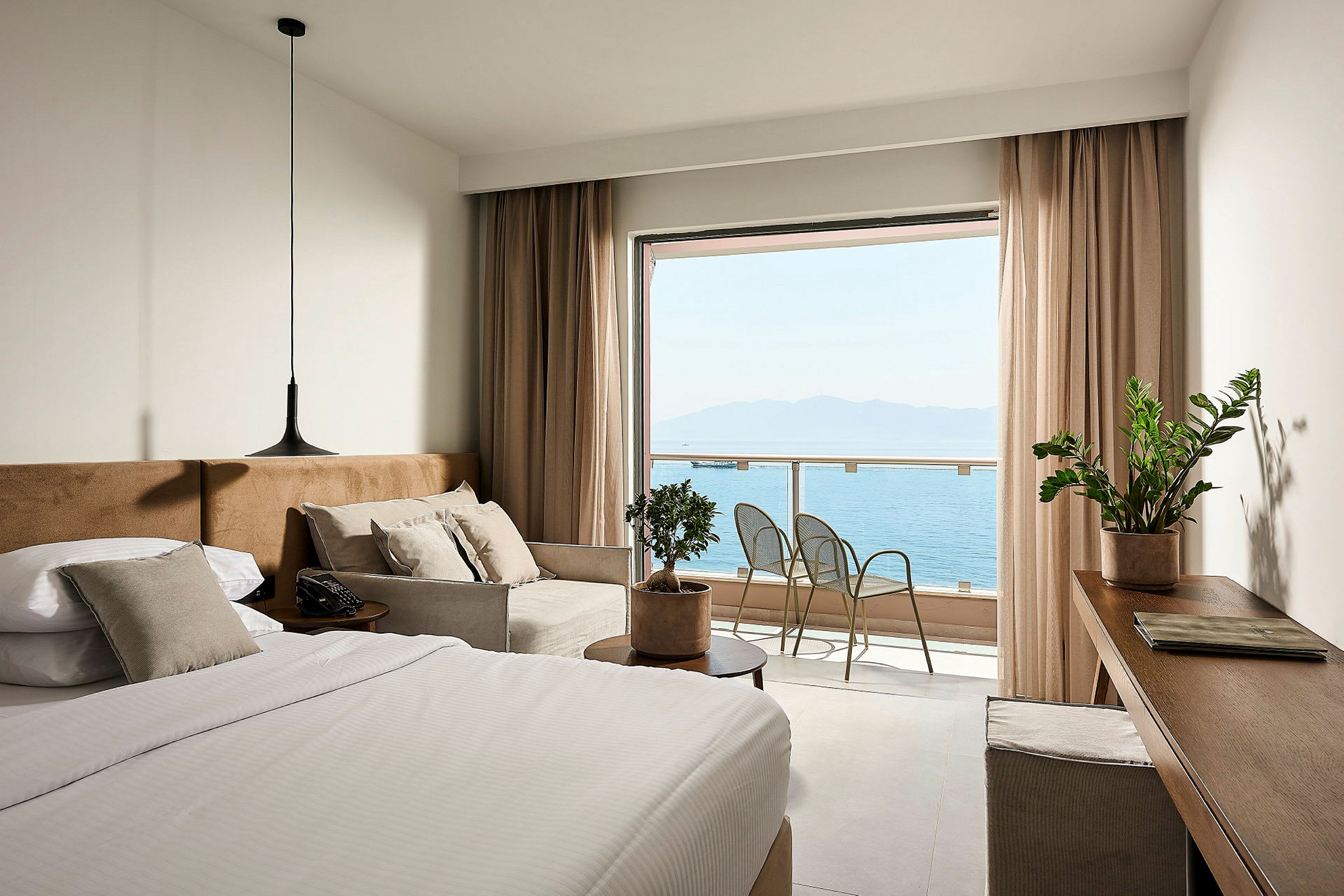 Ett hotellrum med en säng, soffa och utsikt över havet från en balkong. (AI-genererad text)