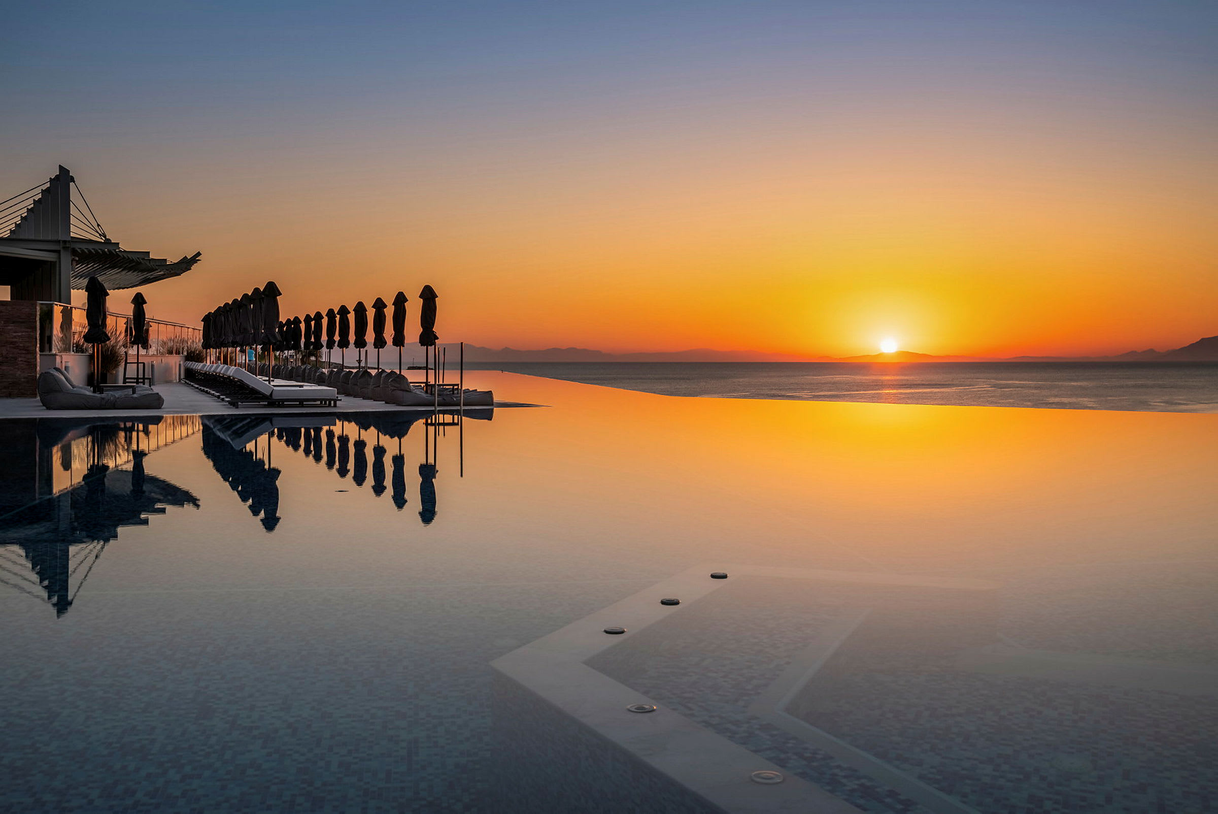 En infinitypool med solstolar och parasoller vid solnedgången. (AI-genererad text)