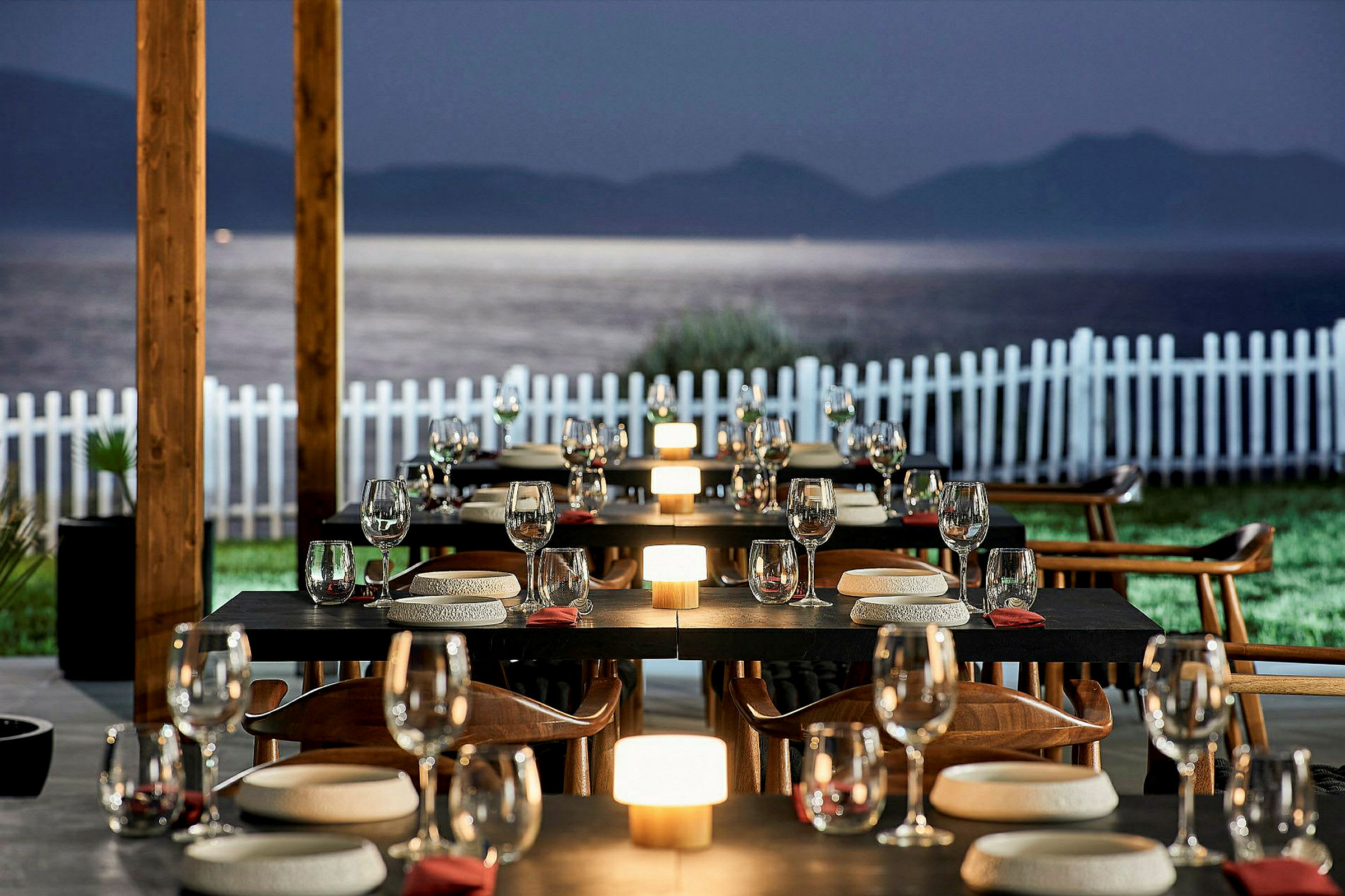 En utomhusrestaurang med dukade bord och utsikt över vatten och berg i bakgrunden. (AI-genererad text)