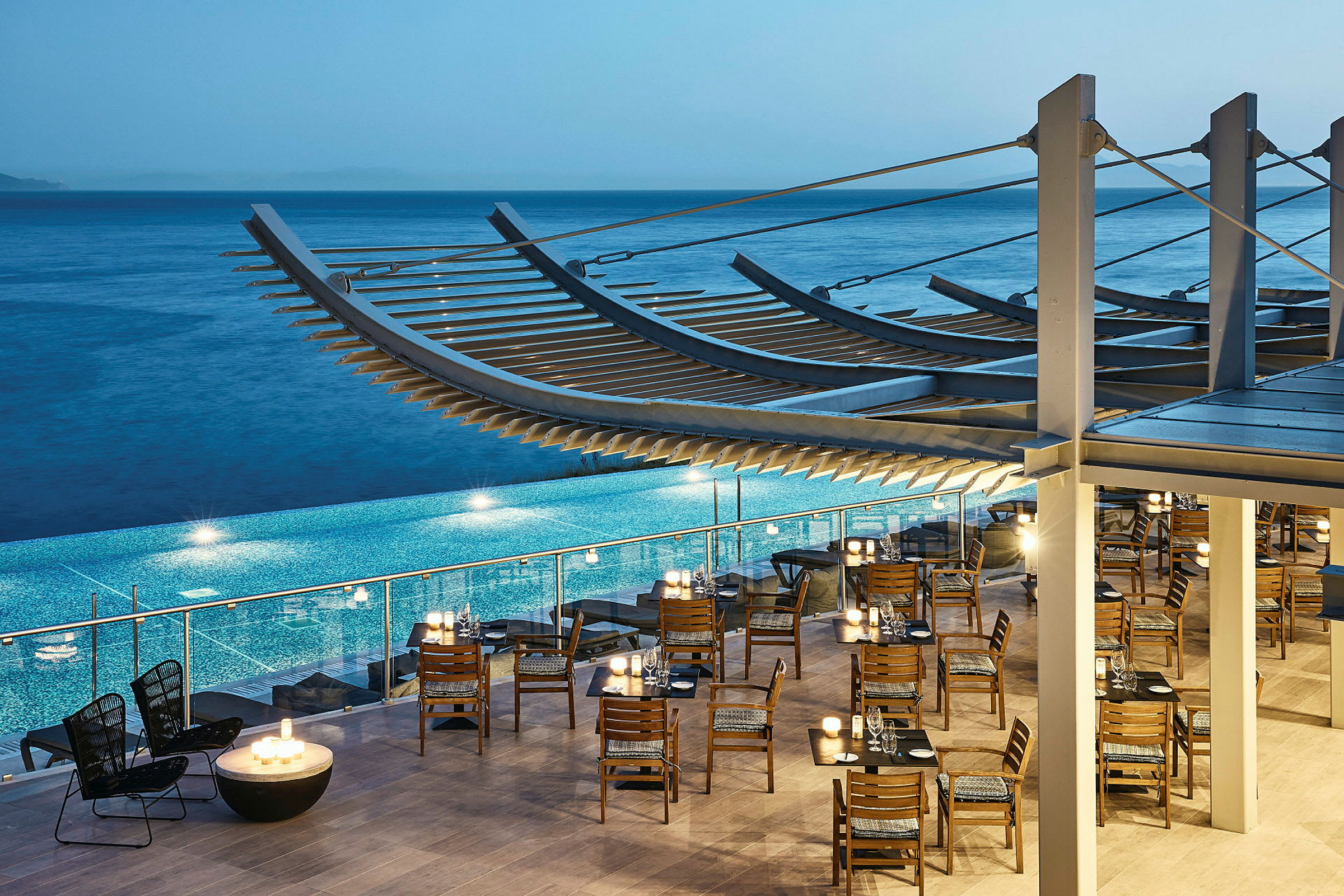 Restaurang med trästolar och bord vid en pool, havet i bakgrunden. (AI-genererad text)