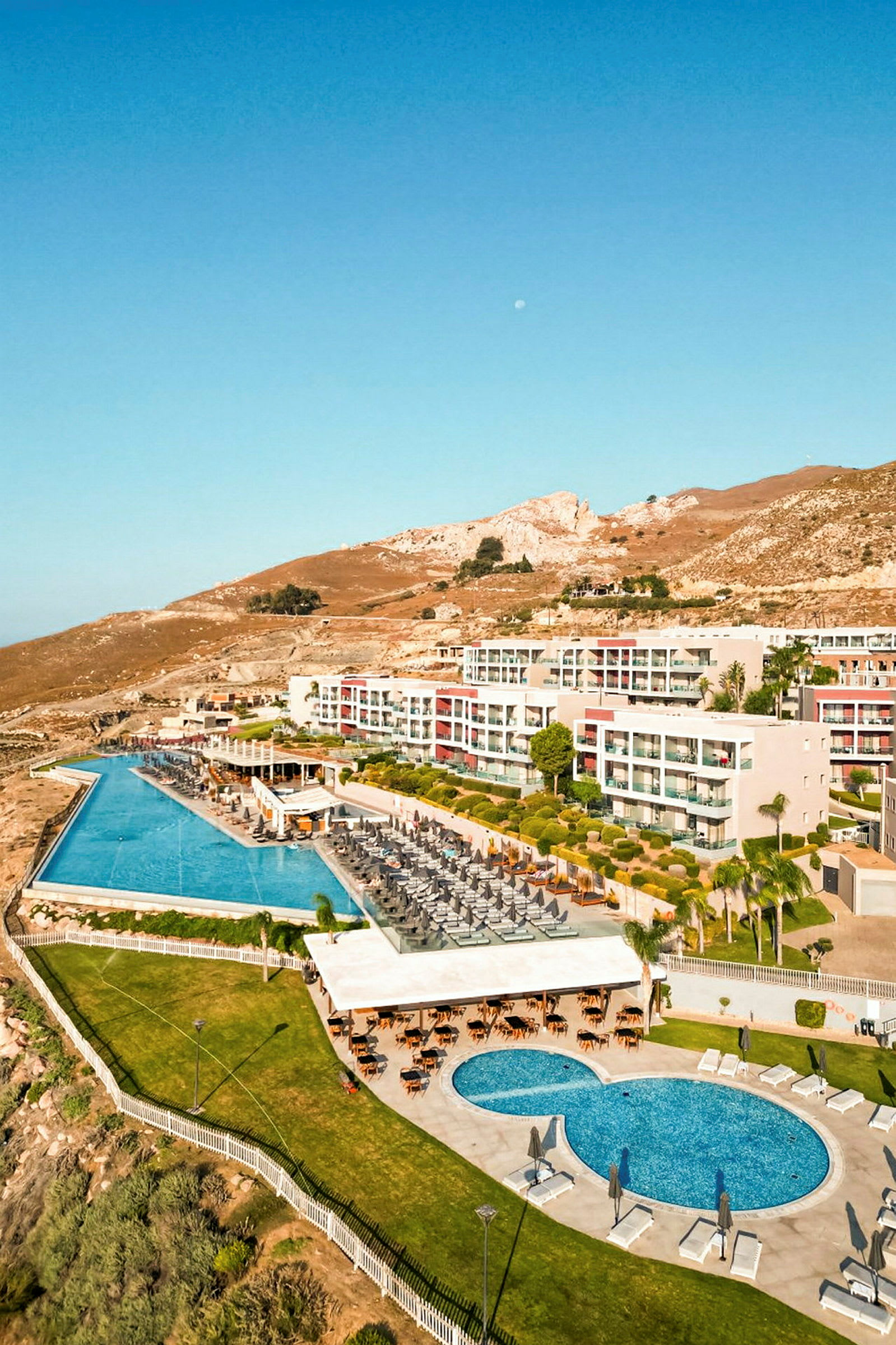 Bild av ett hotellområde med pooler, solstolar och grönska, beläget vid en bergig terräng. (AI-genererad text)
