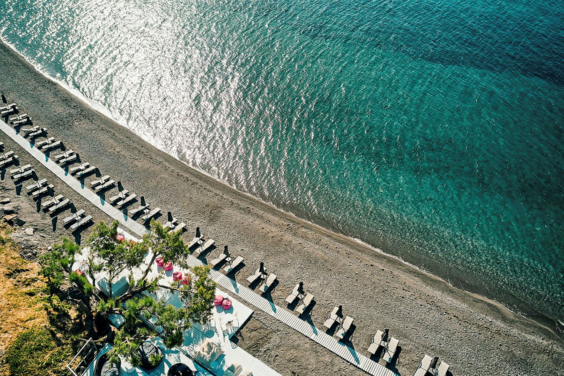 Flygfoto av en strand med solstolar och parasoll samt klart blått hav. (AI-genererad text)