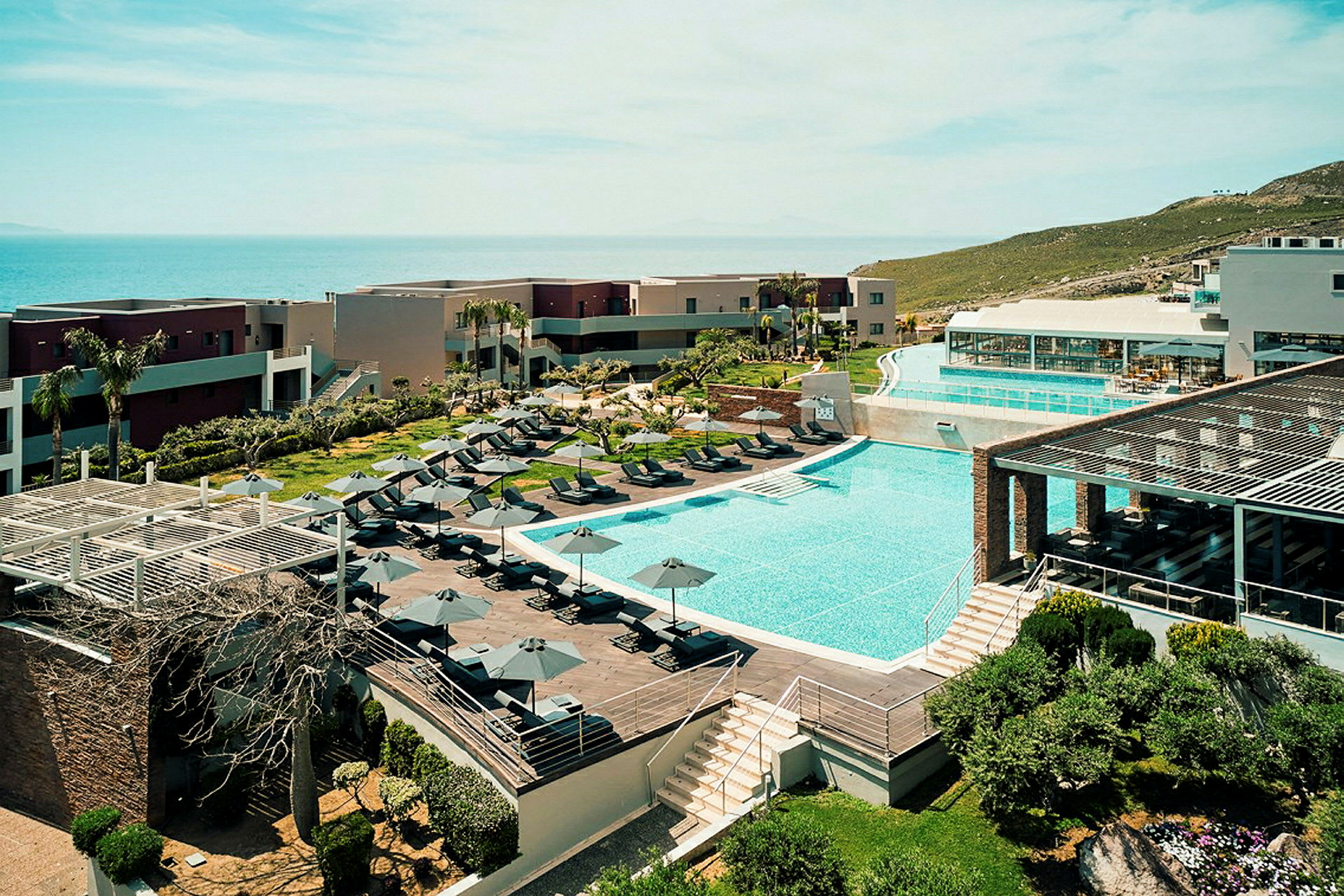Hotellanläggning med pool, solstolar och omgivande byggnader vid havet. (AI-genererad text)