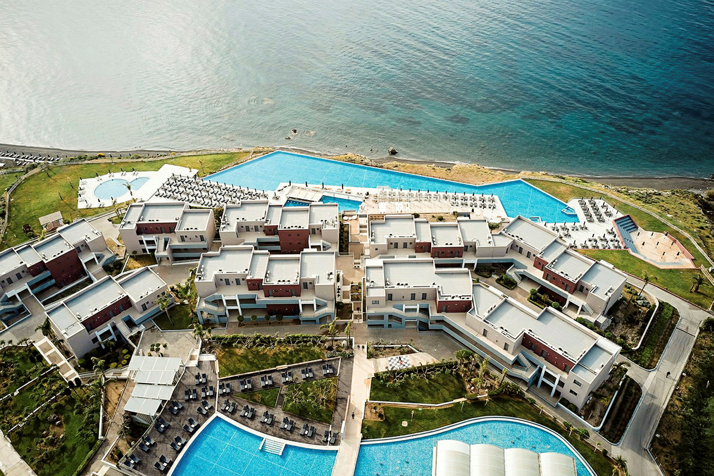 Flygfoto av en hotellanläggning vid havet med pooler och utomhusområden. (AI-genererad text)