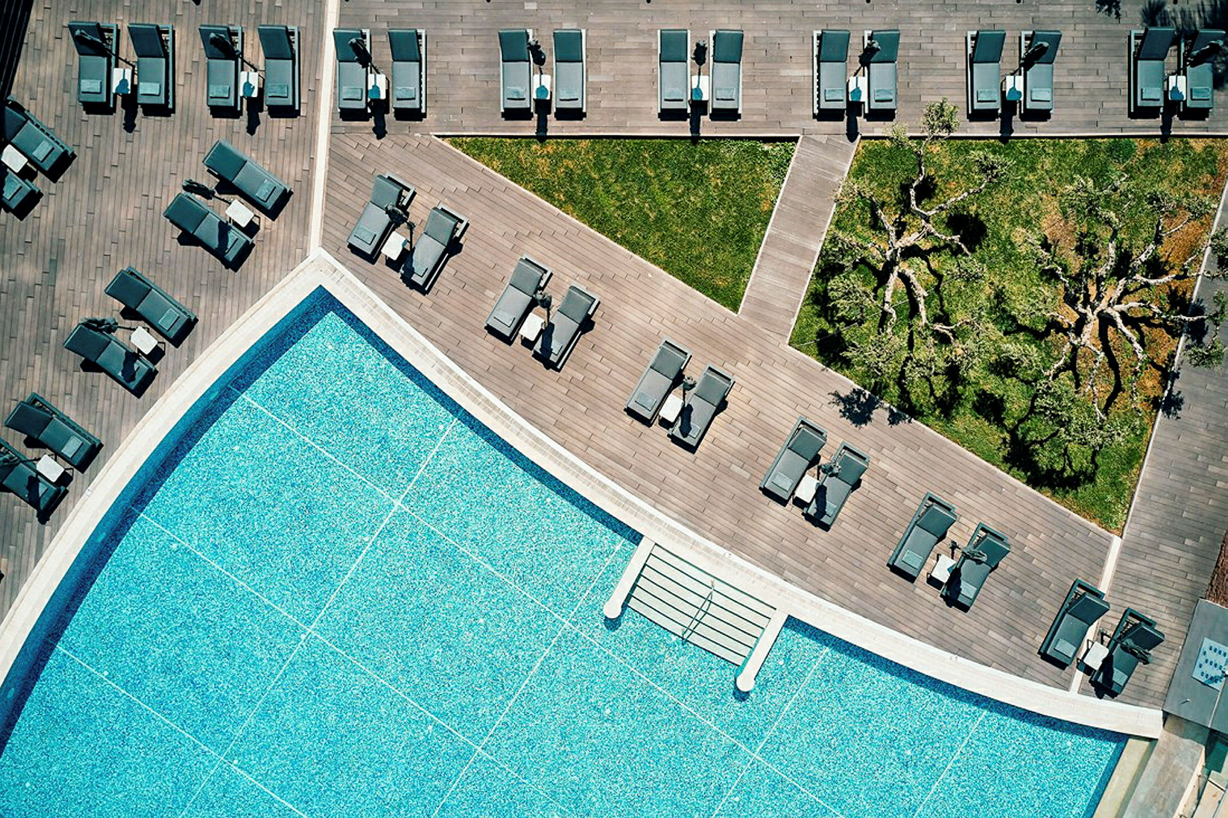 Flygfoto av en swimmingpool, solstolar, träaltan och grönområden. (AI-genererad text)