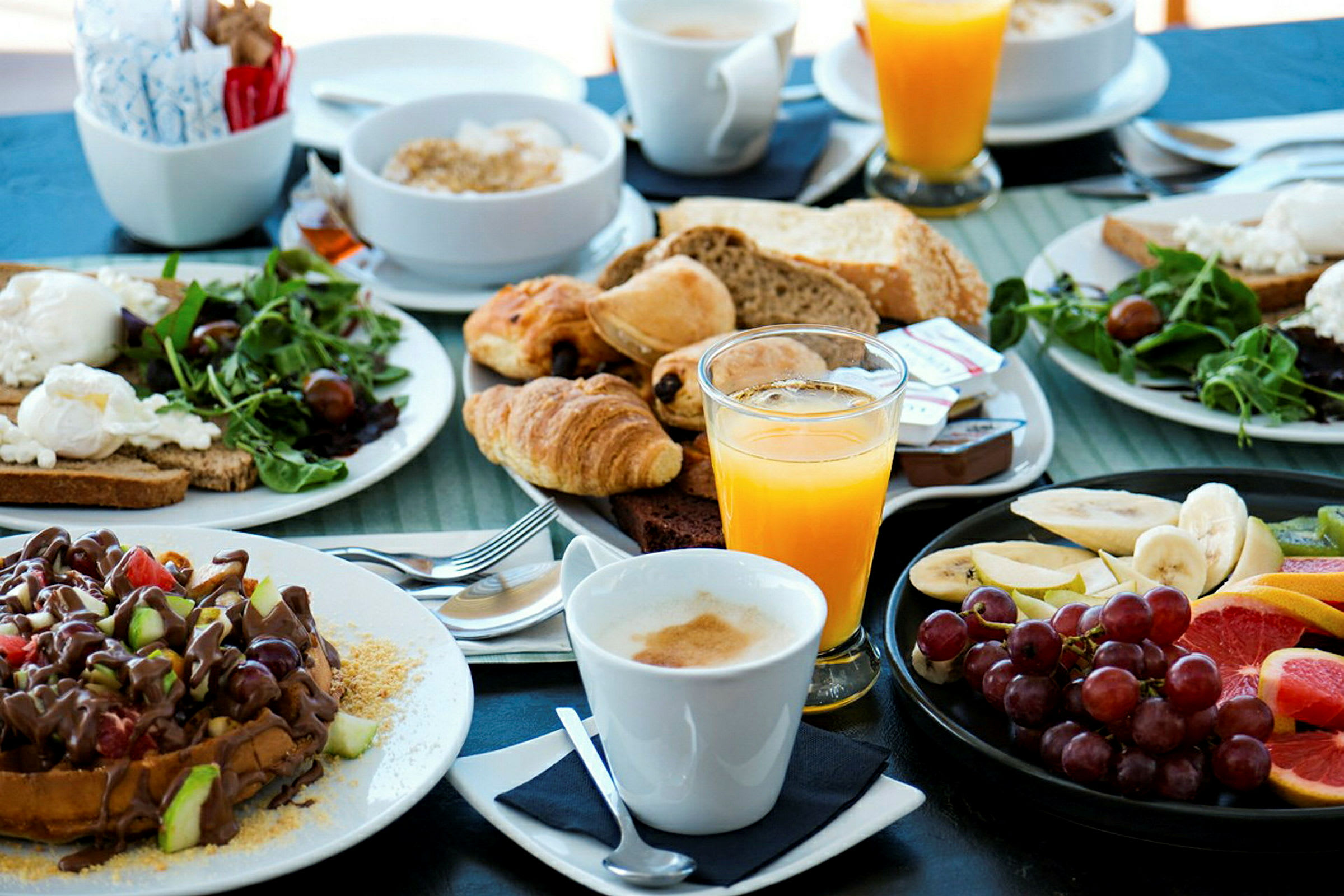 En frukostbuffé med bröd, wienerbröd, frukt, sallad, apelsinjuice och kaffe. (AI-genererad text)