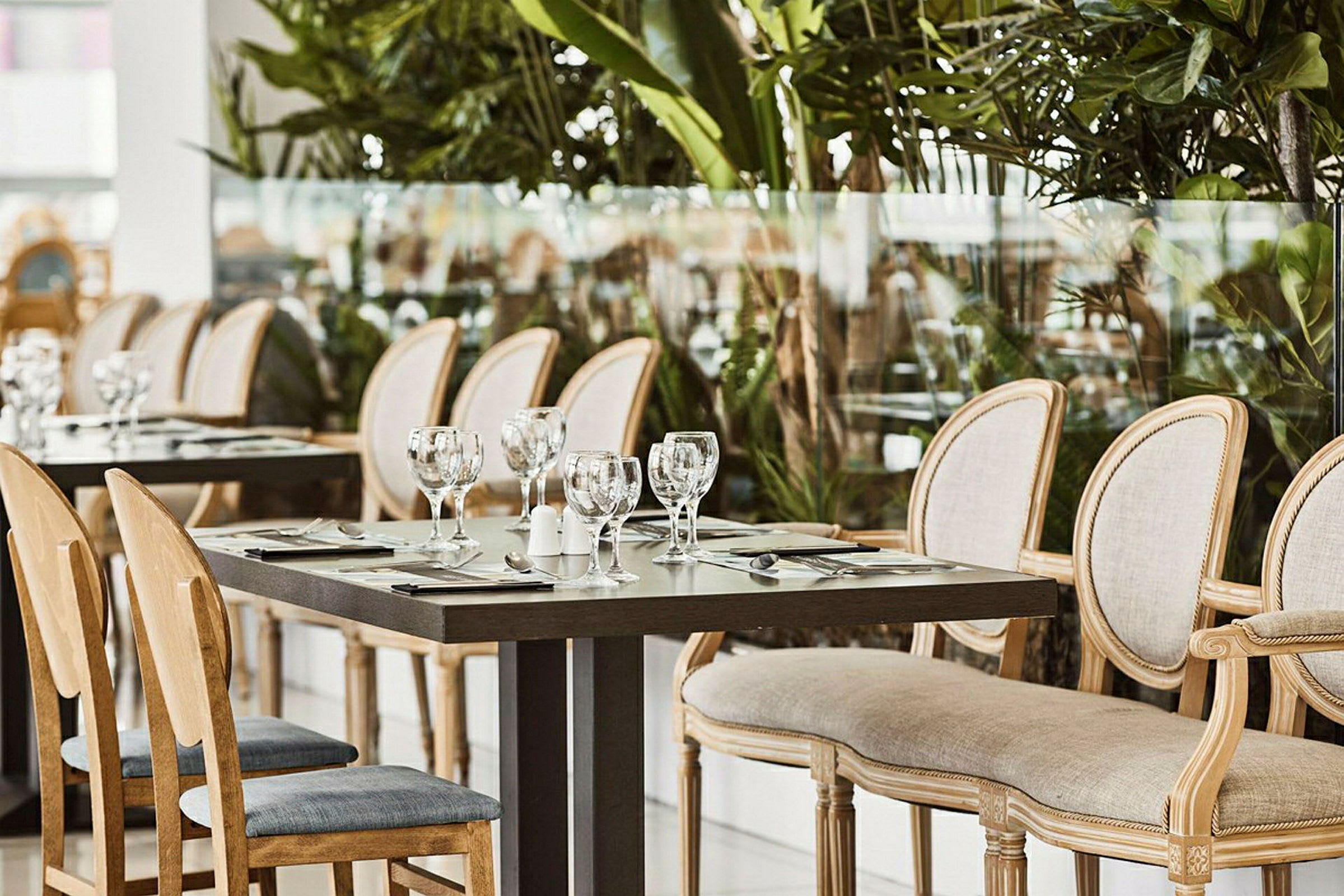 En uppsättning matbord och stolar i en restaurang, omgivna av grönska. (AI-genererad text)