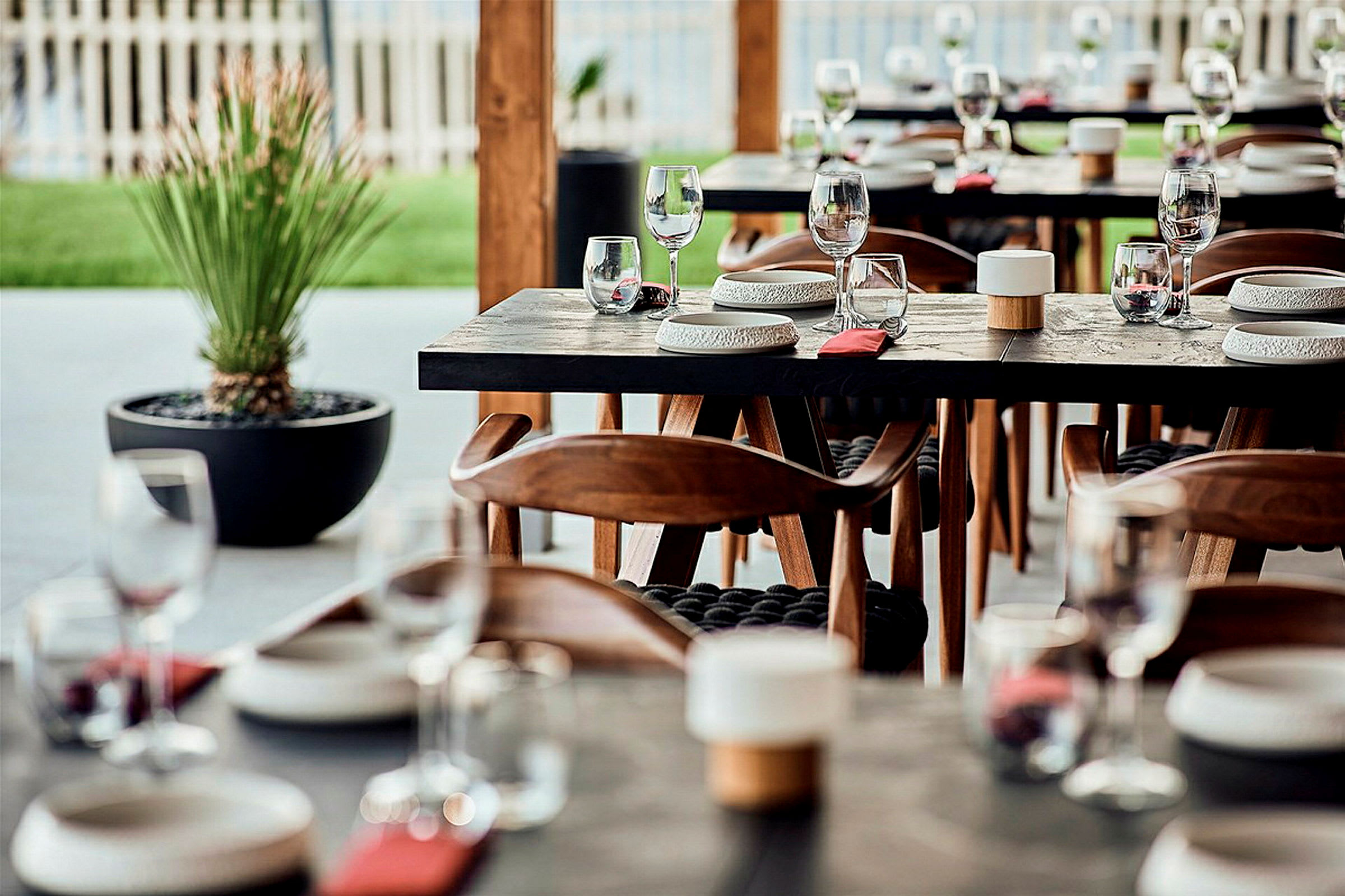 Ett dukat bord med glas och tallrikar i en restaurang med trästolar och en växt i bakgrunden. (AI-genererad text)