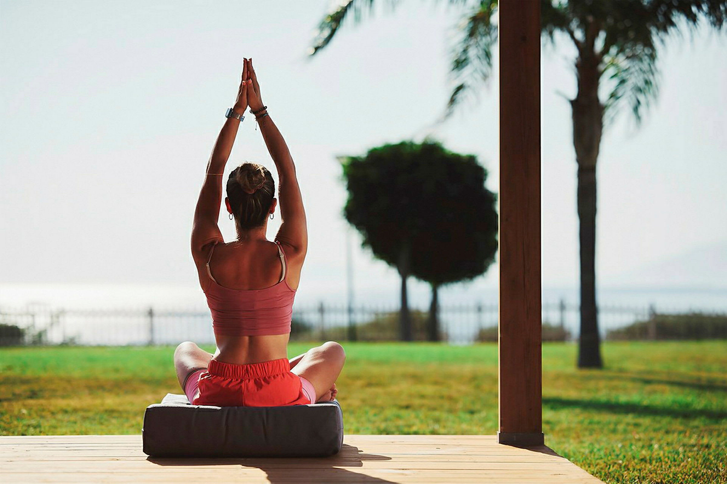 En person utövar yoga med händerna höjda i en sittande position utomhus. (AI-genererad text)