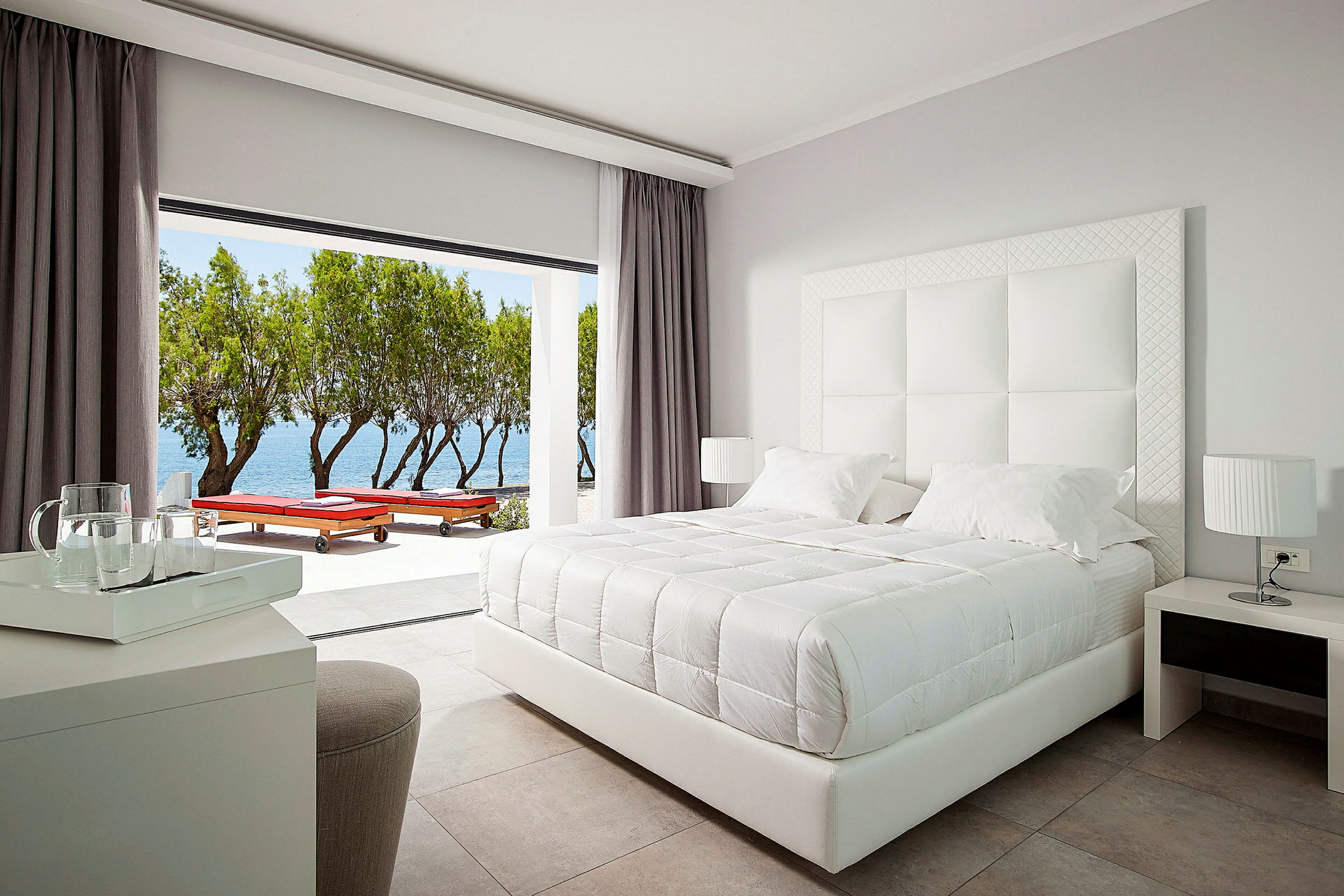 Ett stilrent hotellrum med en vit dubbelsäng och utsikt mot havet. (AI-genererad text)
