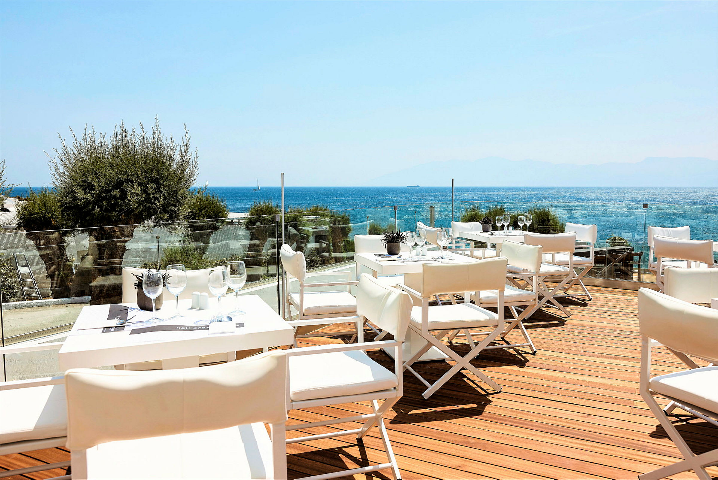 En terrass med vita bord och stolar, utsikt över havet. (AI-genererad text)