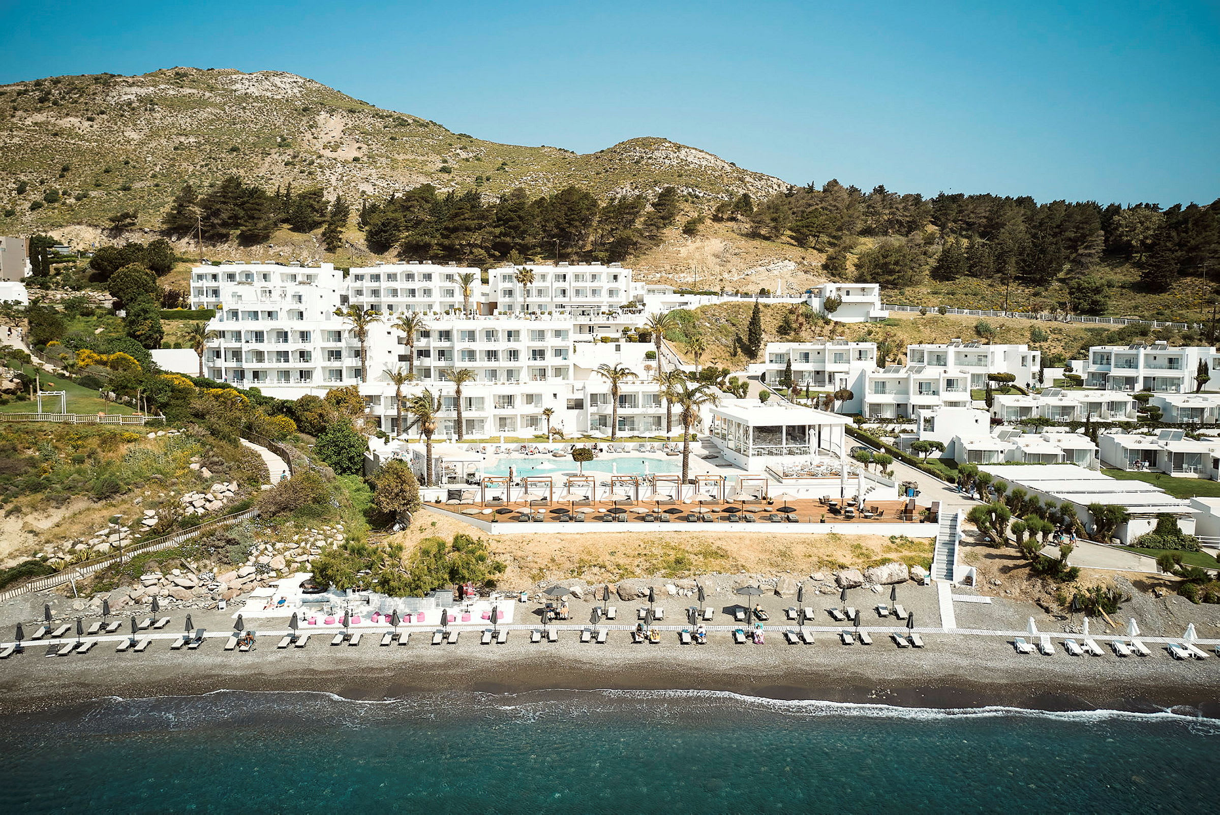 Hotellkomplex vid stranden med poolområde och omgivande grönska. (AI-genererad text)