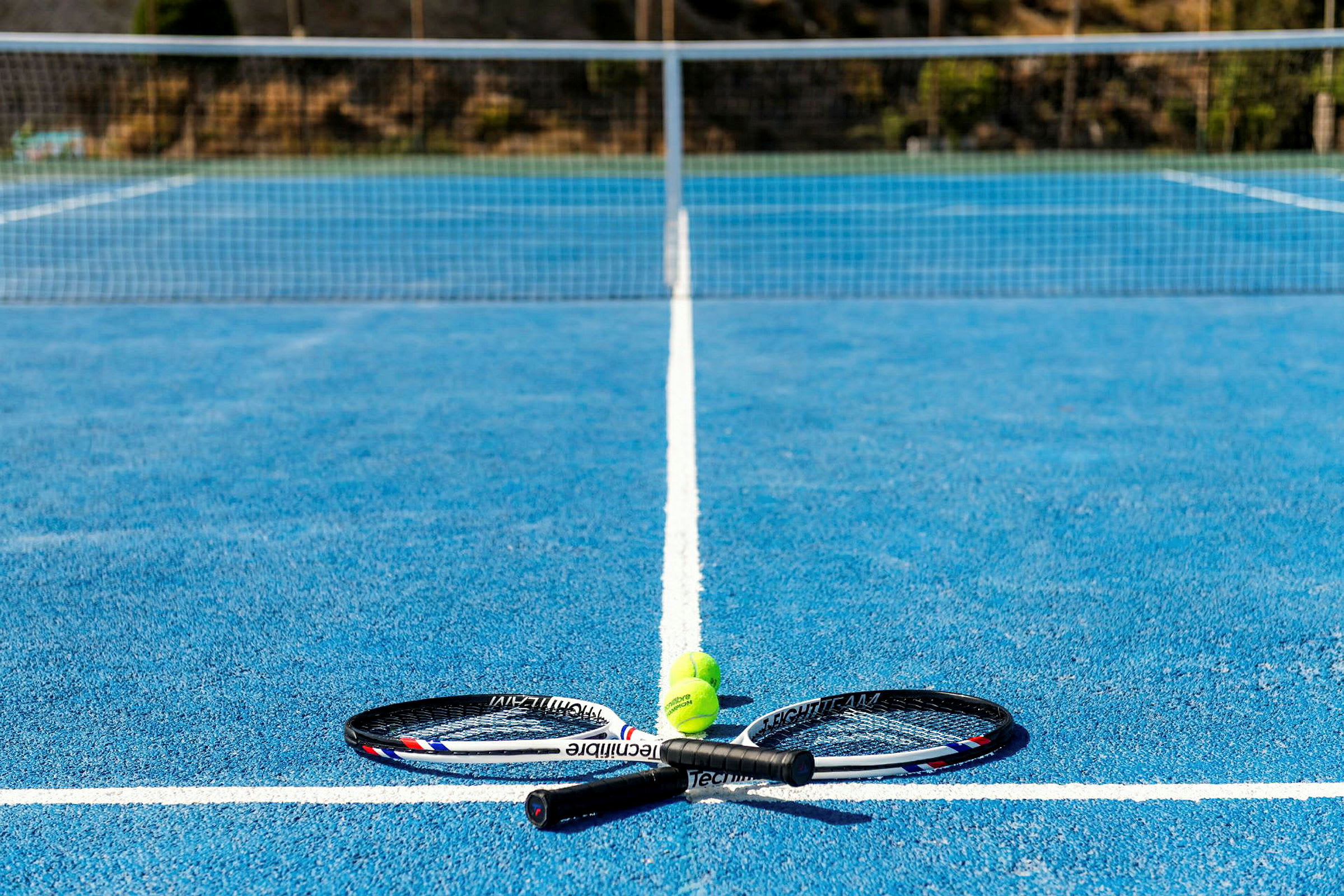 Två tennisracketar och tre tennisbollar på en blå tennisbana. (AI-genererad text)