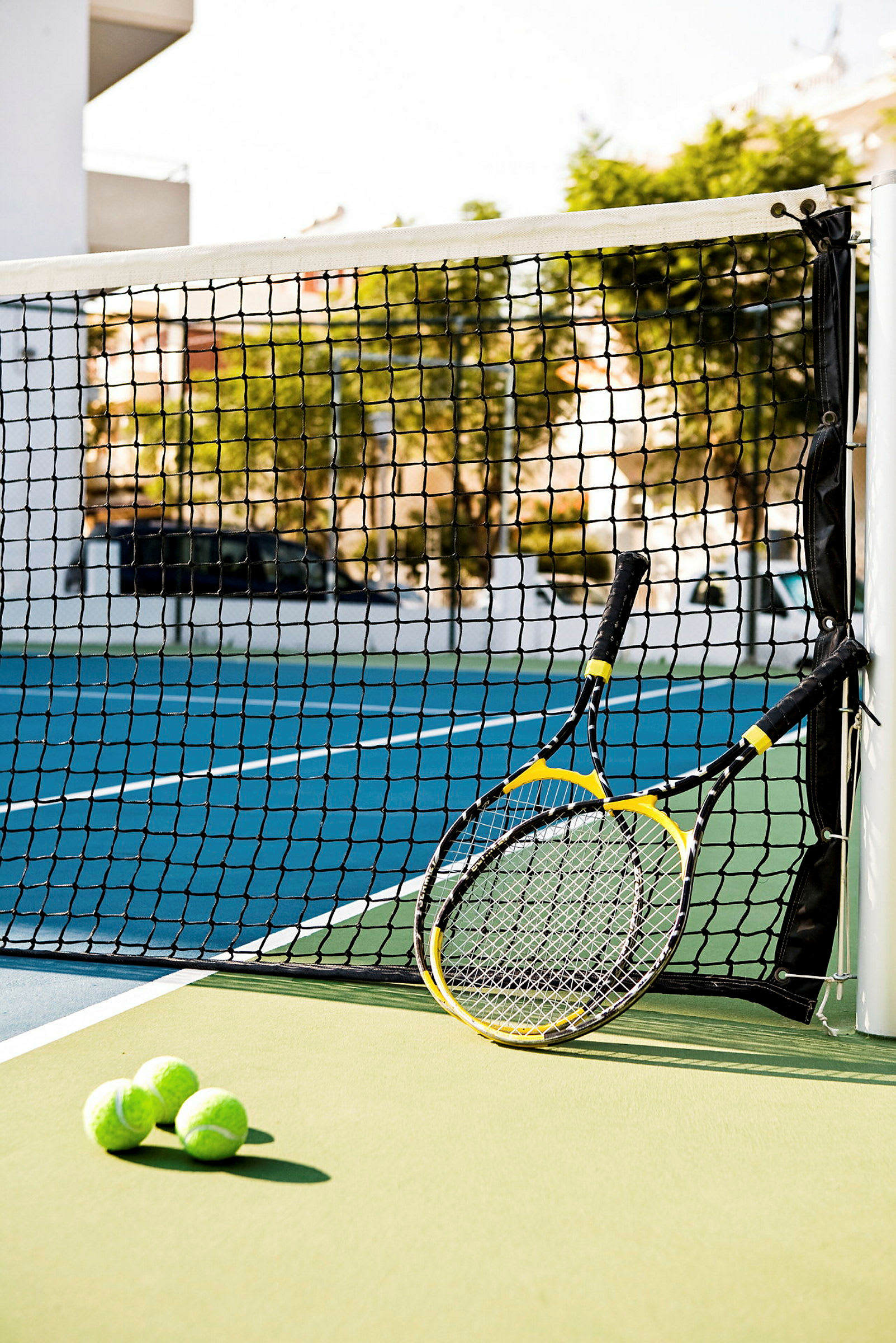 Två tennisracketar och tre tennisbollar vid ett nät på en tennisbana. (AI-genererad text)