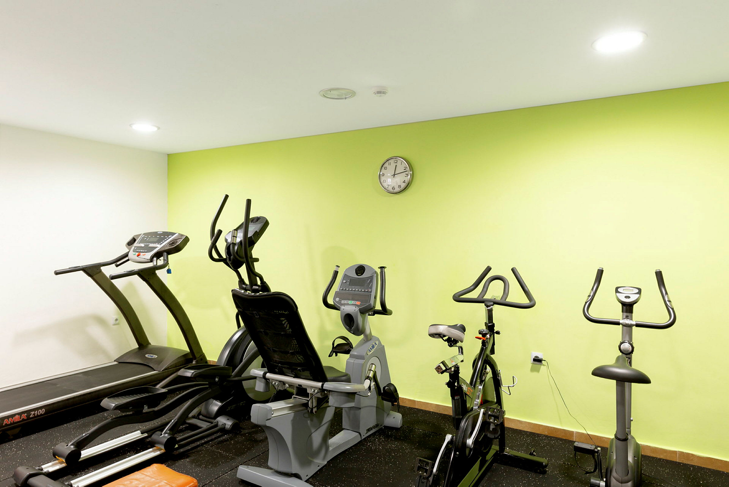 Bild av ett gym med träningsmaskiner mot en grön vägg. (AI-genererad text)