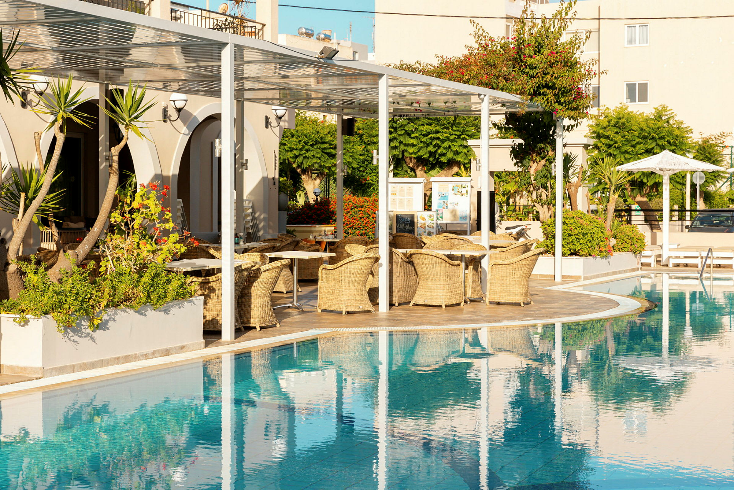 Hotellpool med sittplatser och grönska i bakgrunden. (AI-genererad text)