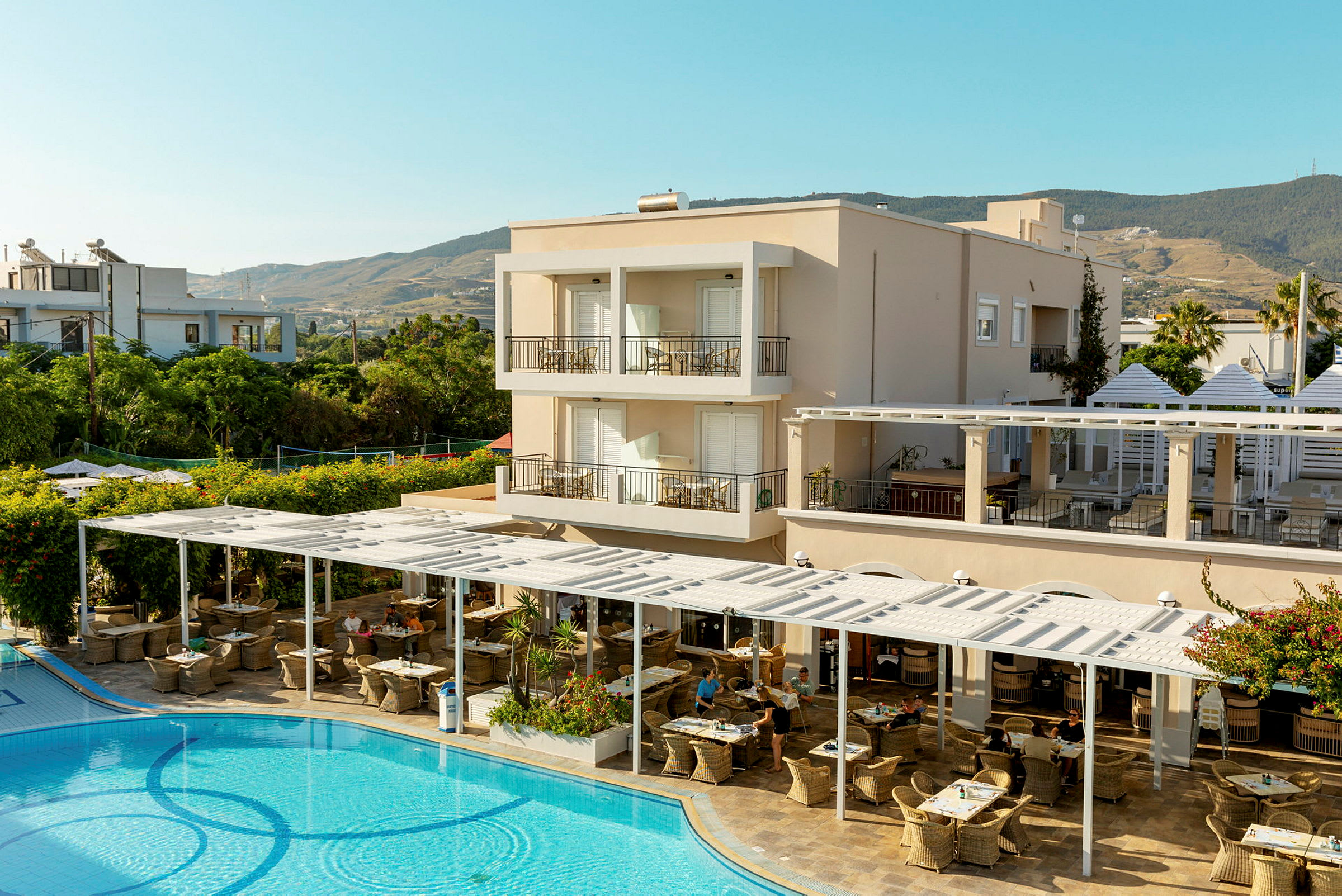 En hotellbyggnad med balkonger, en utomhusrestaurang och en pool i förgrunden. (AI-genererad text)