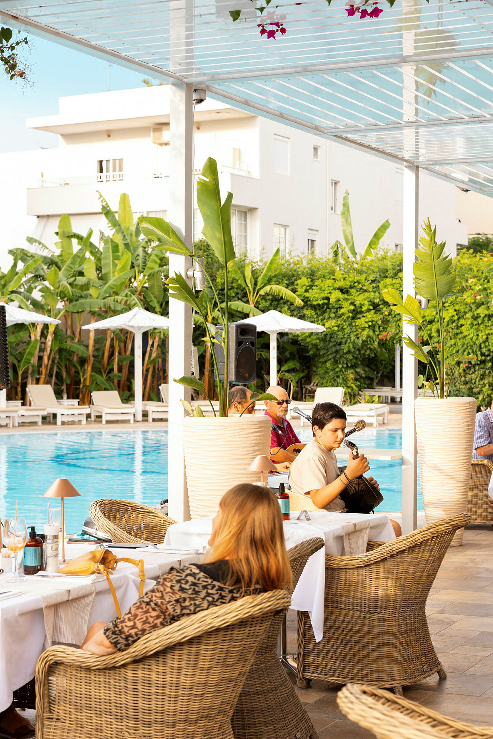 Personer sitter vid bord bredvid en pool under tak. (AI-genererad text)