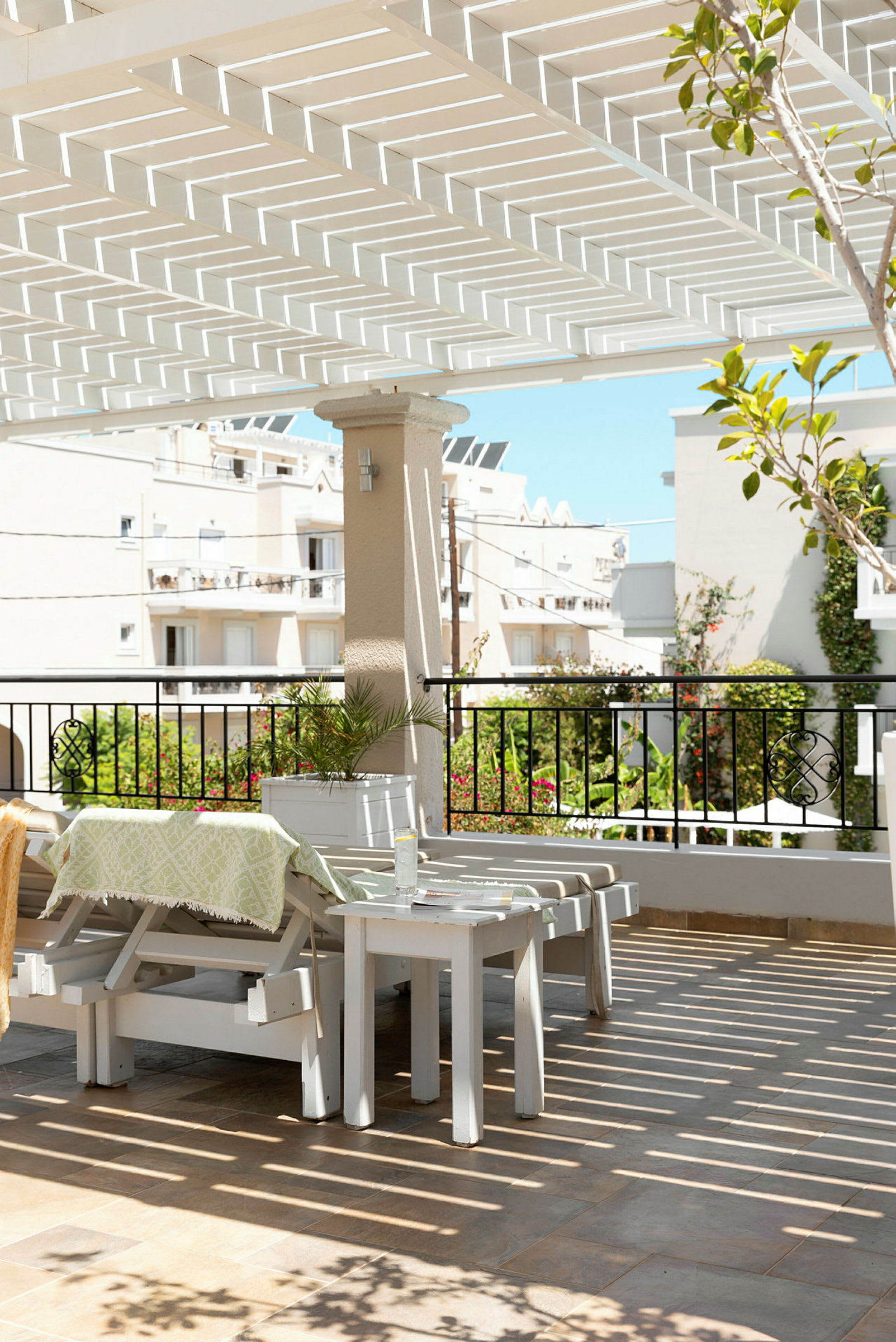 Utomhusområde med vit pergola, utemöbler och vy mot byggnader och grönska. (AI-genererad text)